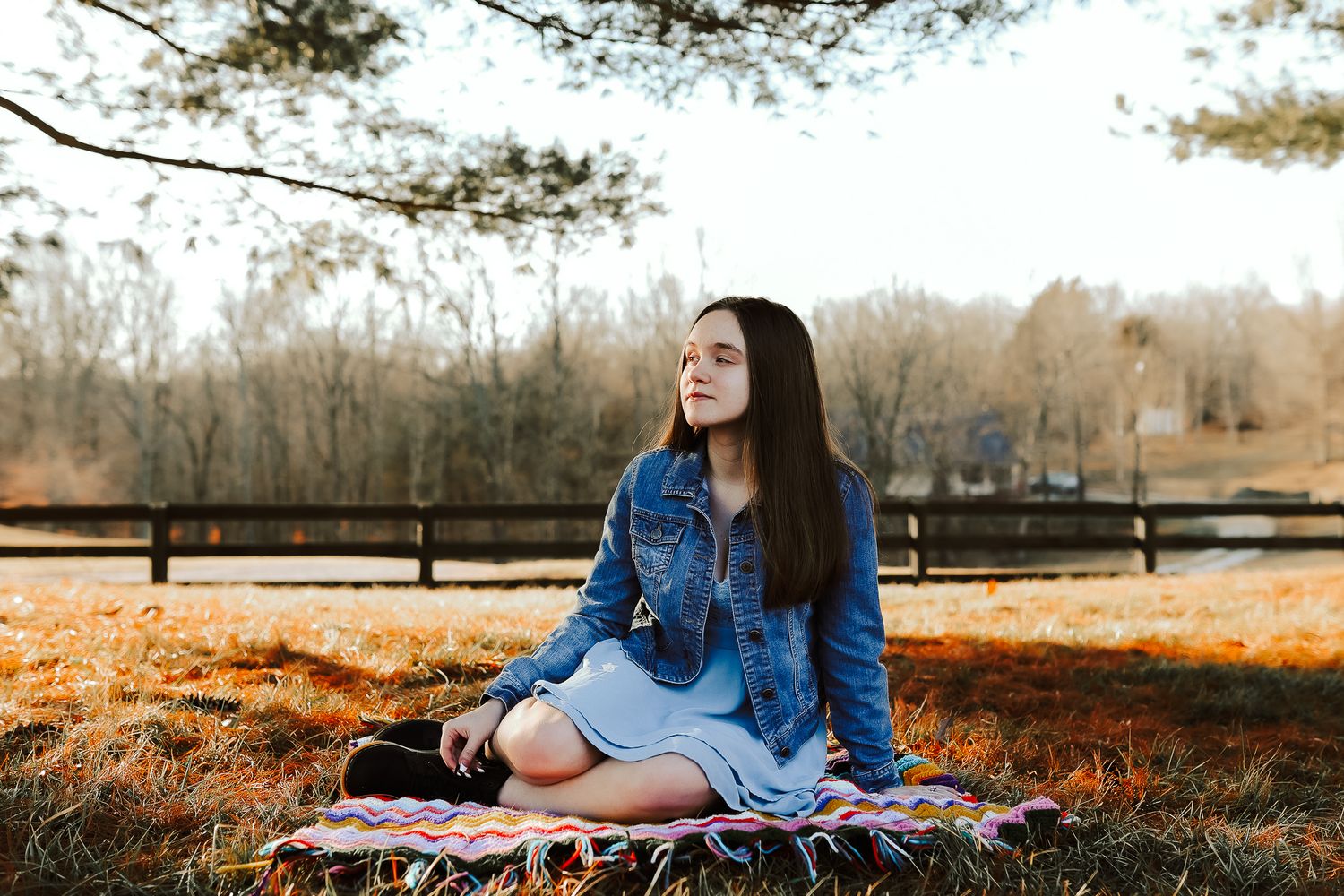 A peaceful autumn scene with someone sitting on a blanket near a rustic fence.