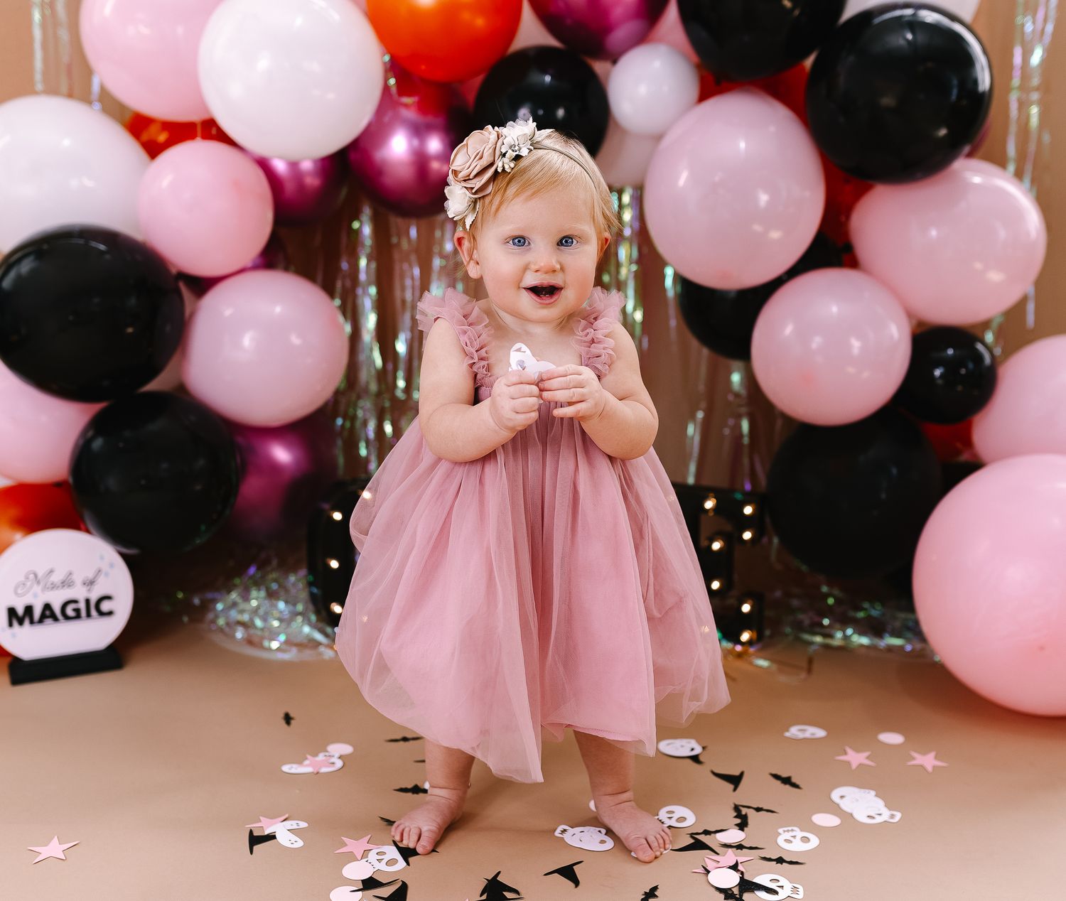 A festive celebration with pink and black balloon arch and confetti on wooden floor.