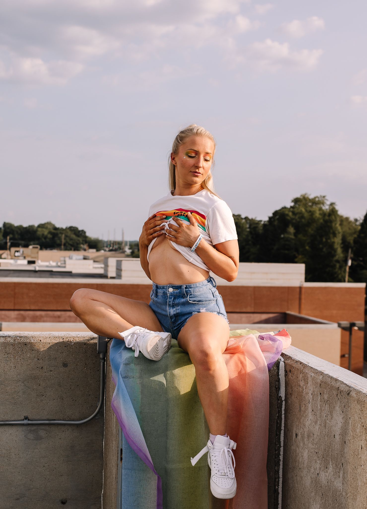 Casual summer rooftop portrait in denim shorts and white sneakers against urban backdrop.