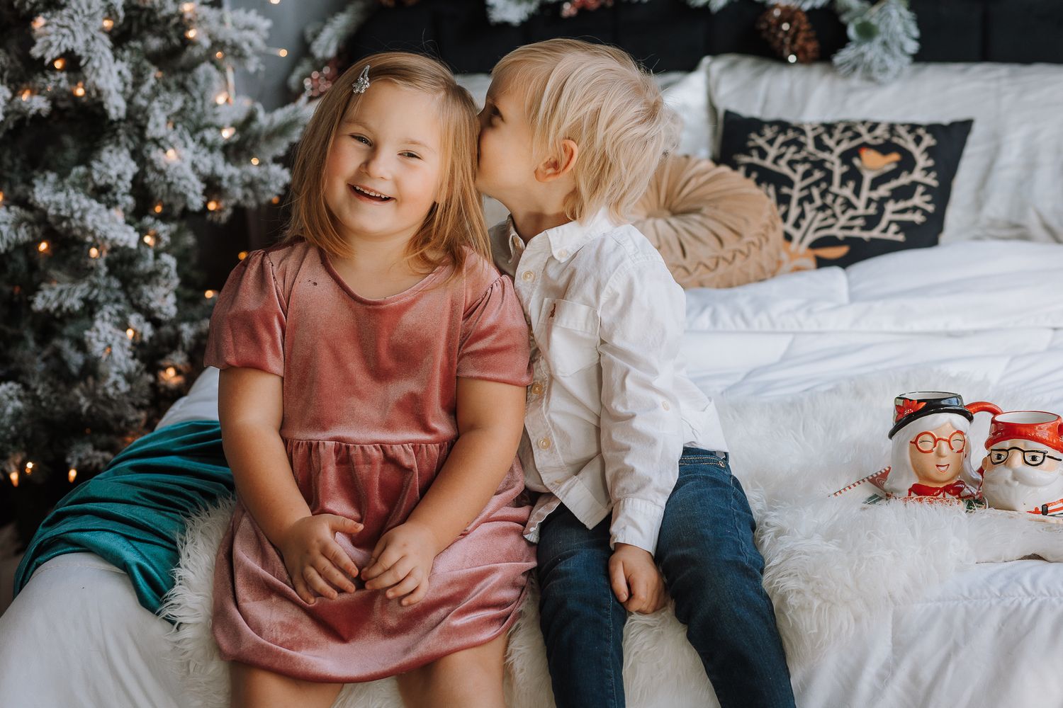 Two children share a sweet candid moment near a decorated Christmas tree.