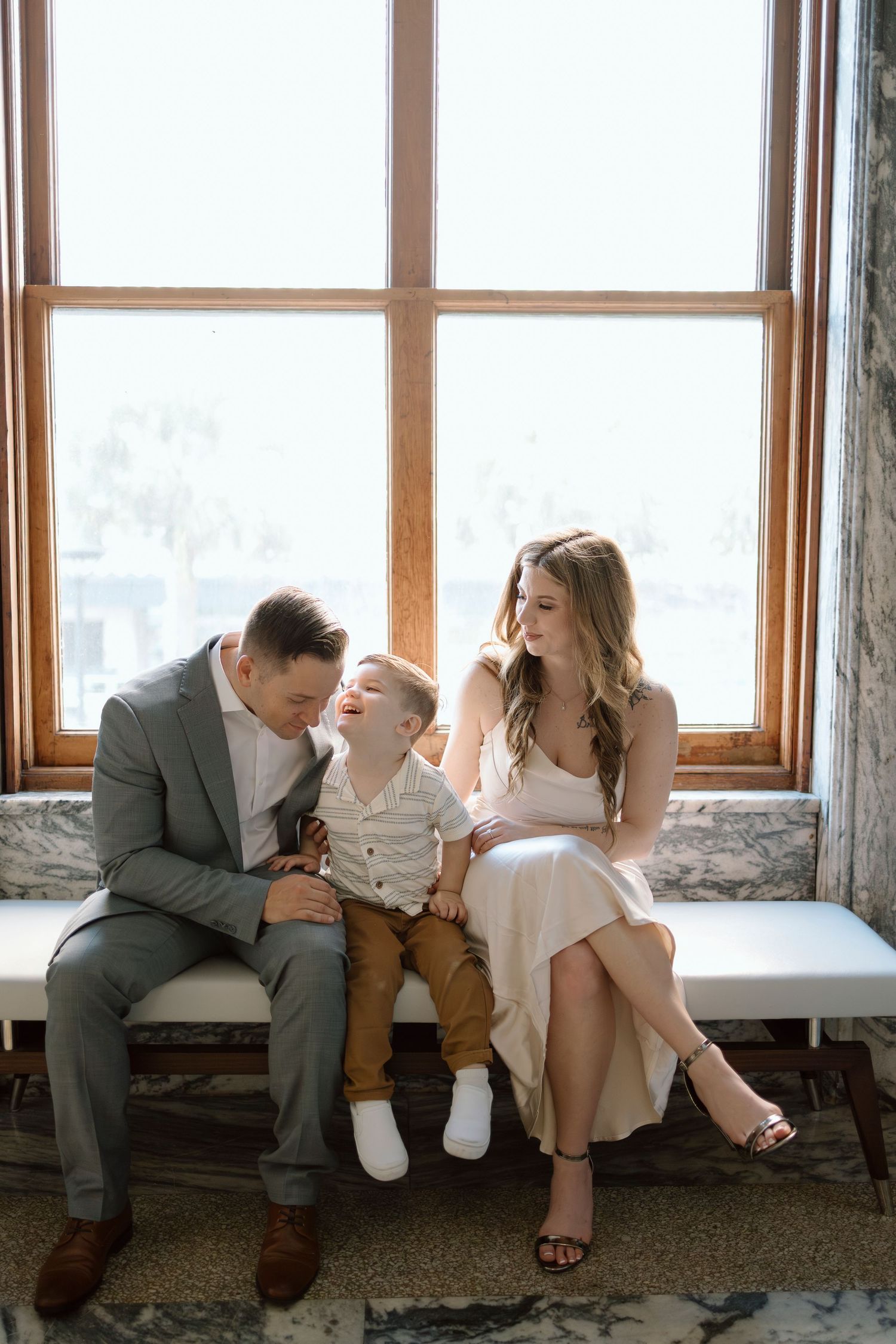 Family sitting together by a bright window in formal attire share a tender moment.