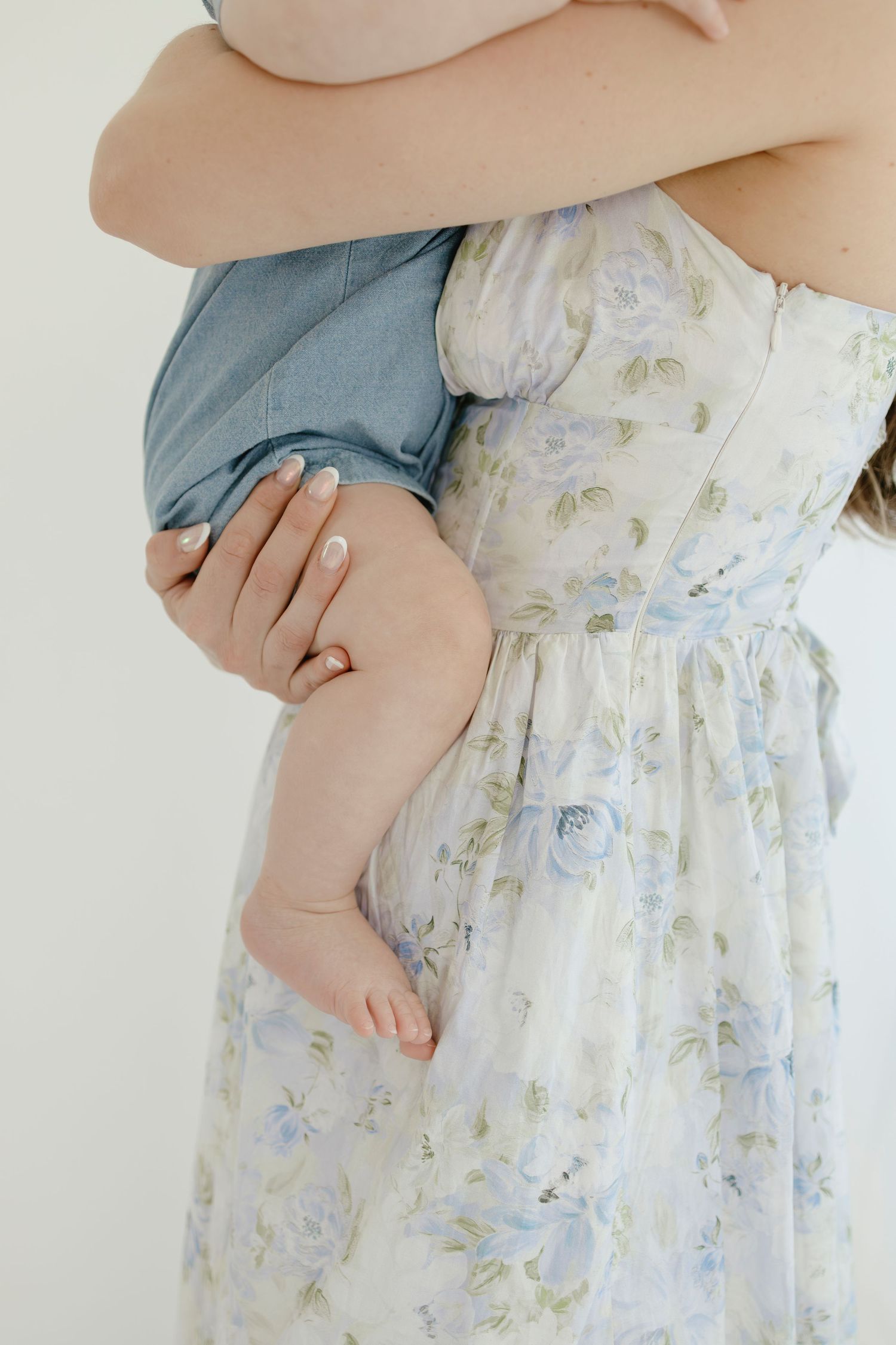 Close-up of tiny baby feet and floral dress details in studio setting.