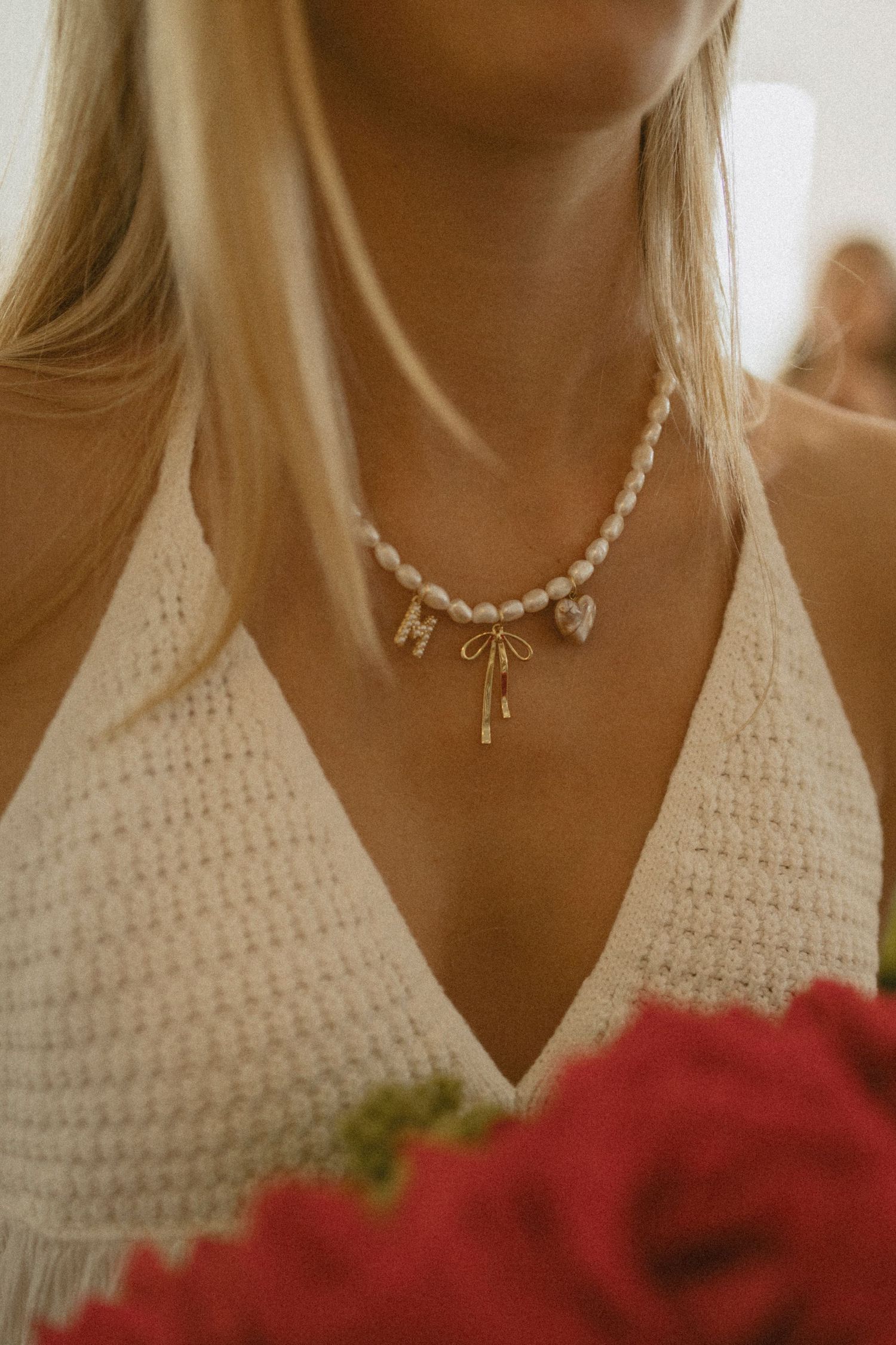 Pearl charm necklace on person wearing white crochet top with red roses in foreground.