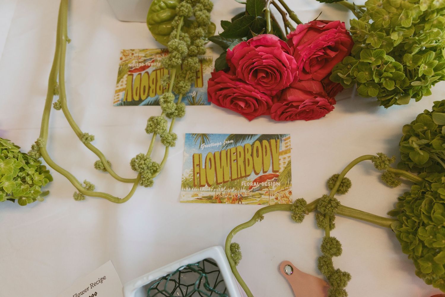 Floral arrangement supplies with red roses, green hydrangeas and event tickets on white surface.