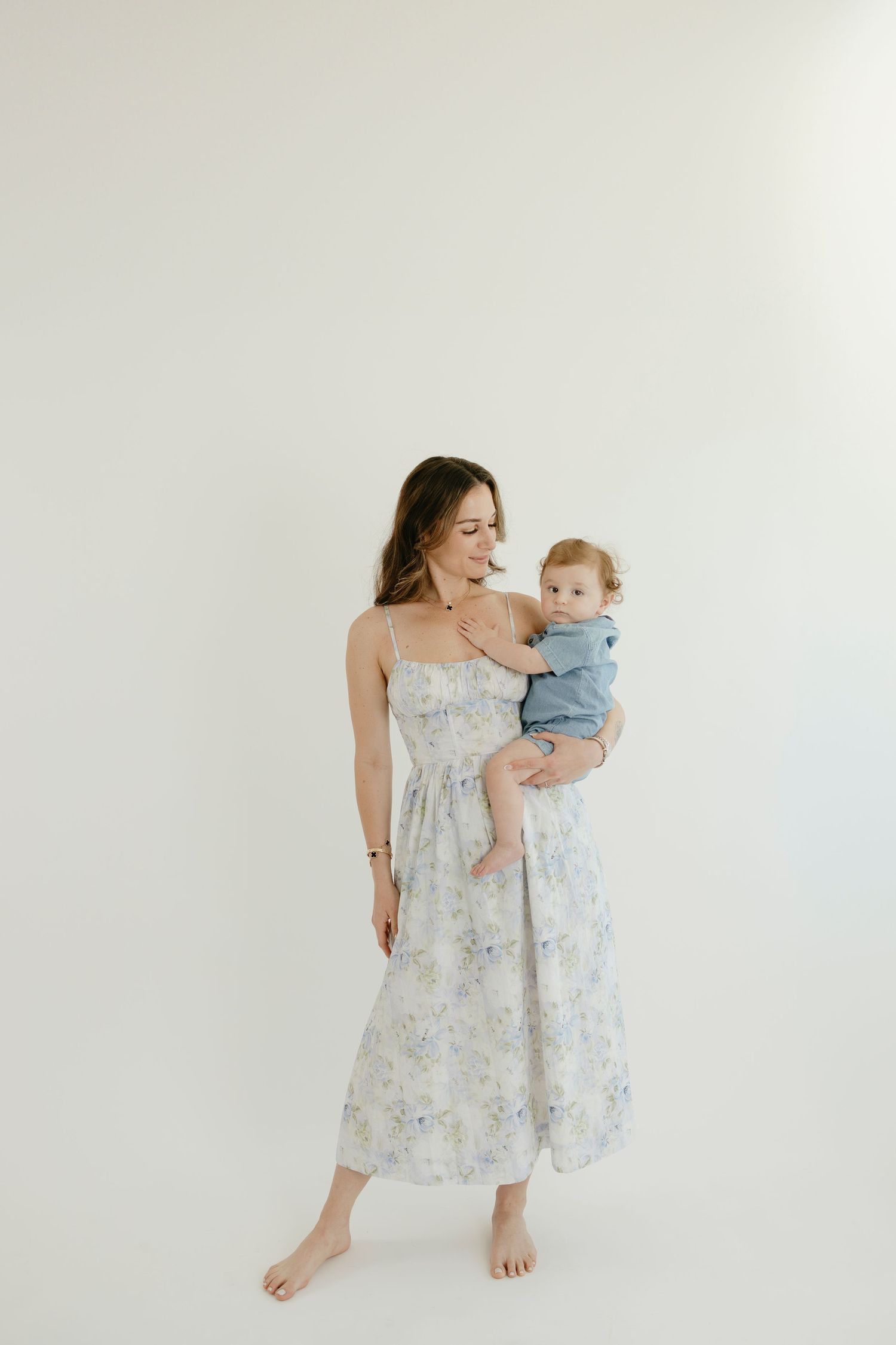 Parent and baby in coordinating blue and floral outfits pose in minimalist studio setting.