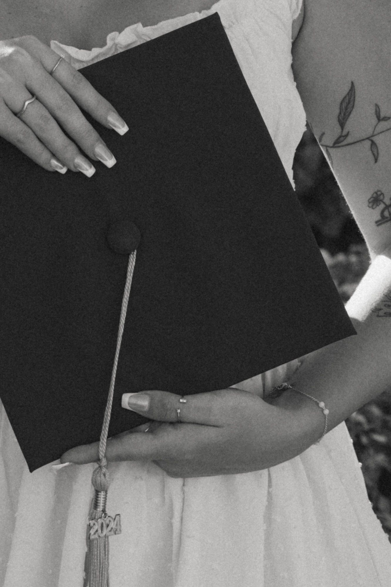 Black and white close-up of hands holding a graduation cap with tassel.