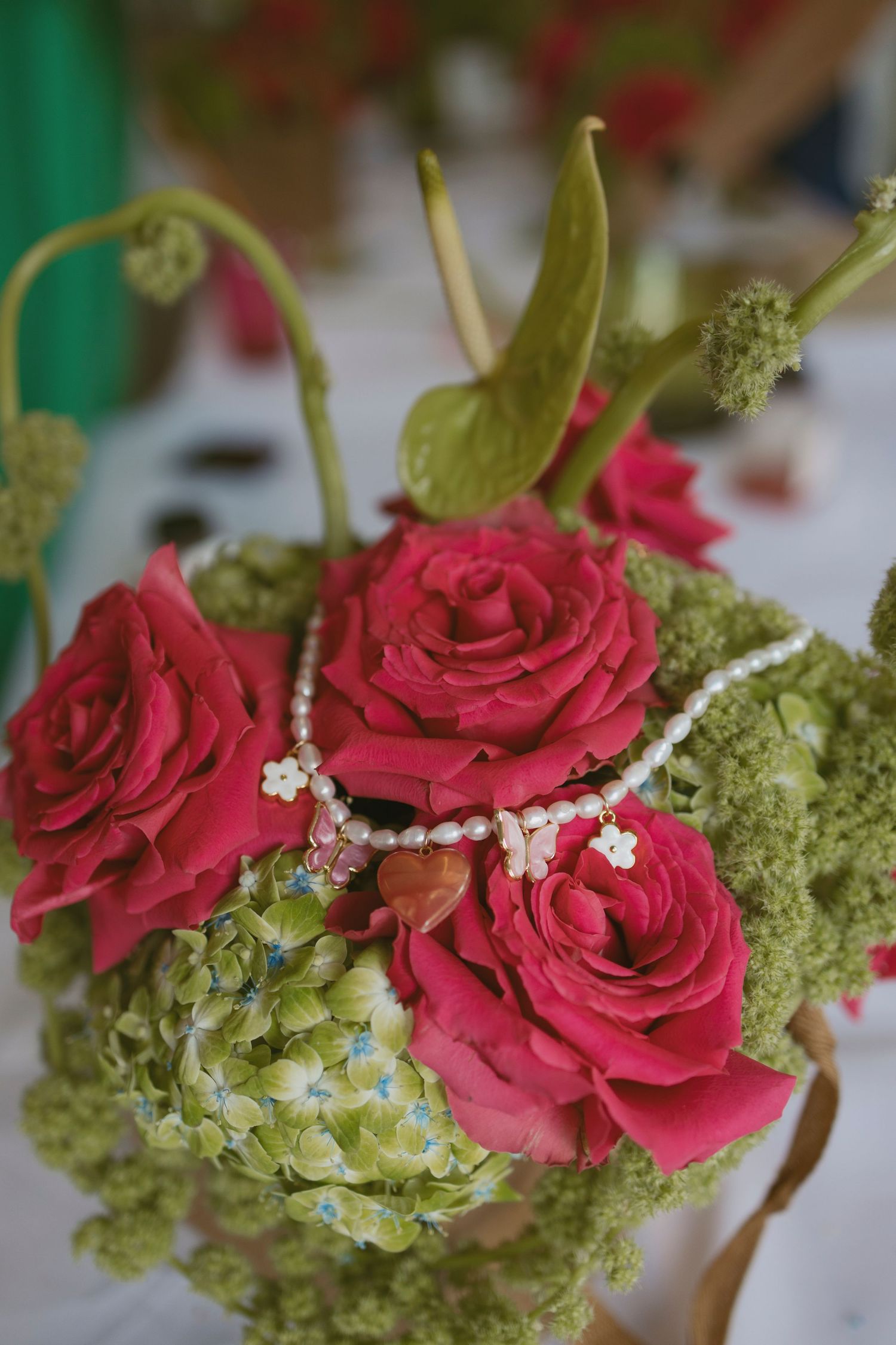 Close-up of elegant floral arrangement with red roses, green hydrangeas and pearl necklace accents.