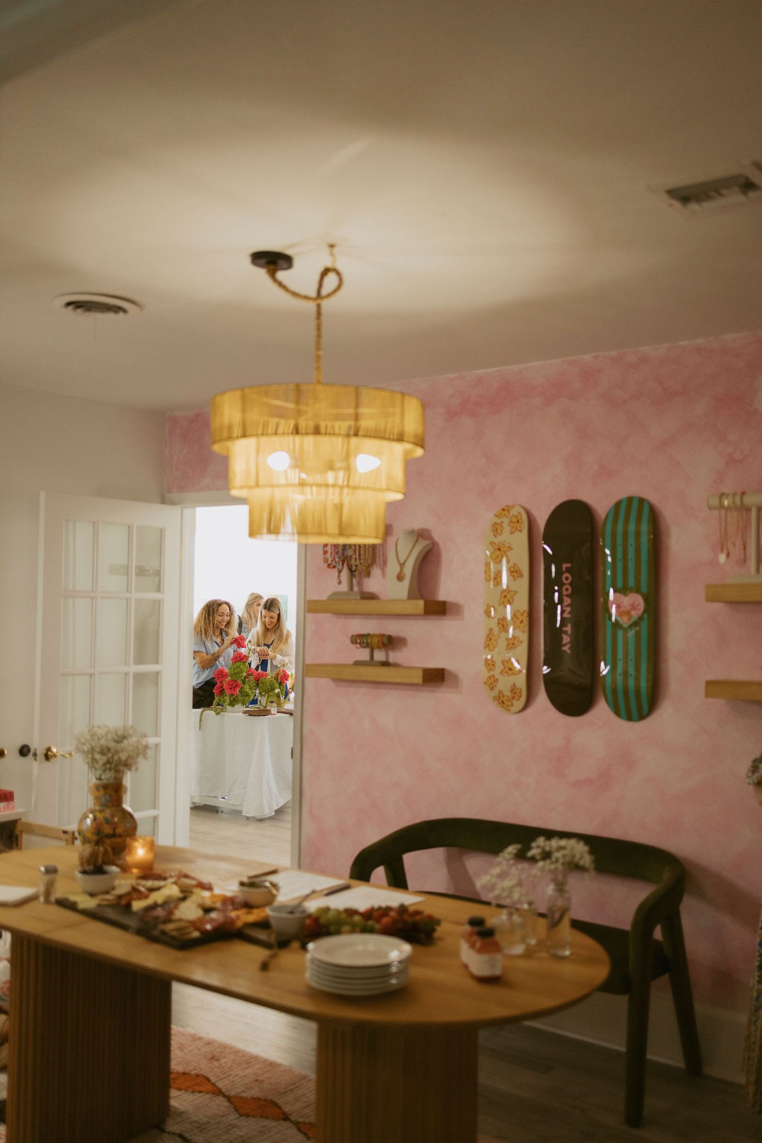 Dining room with pink textured walls and wooden table under gold tiered chandelier.