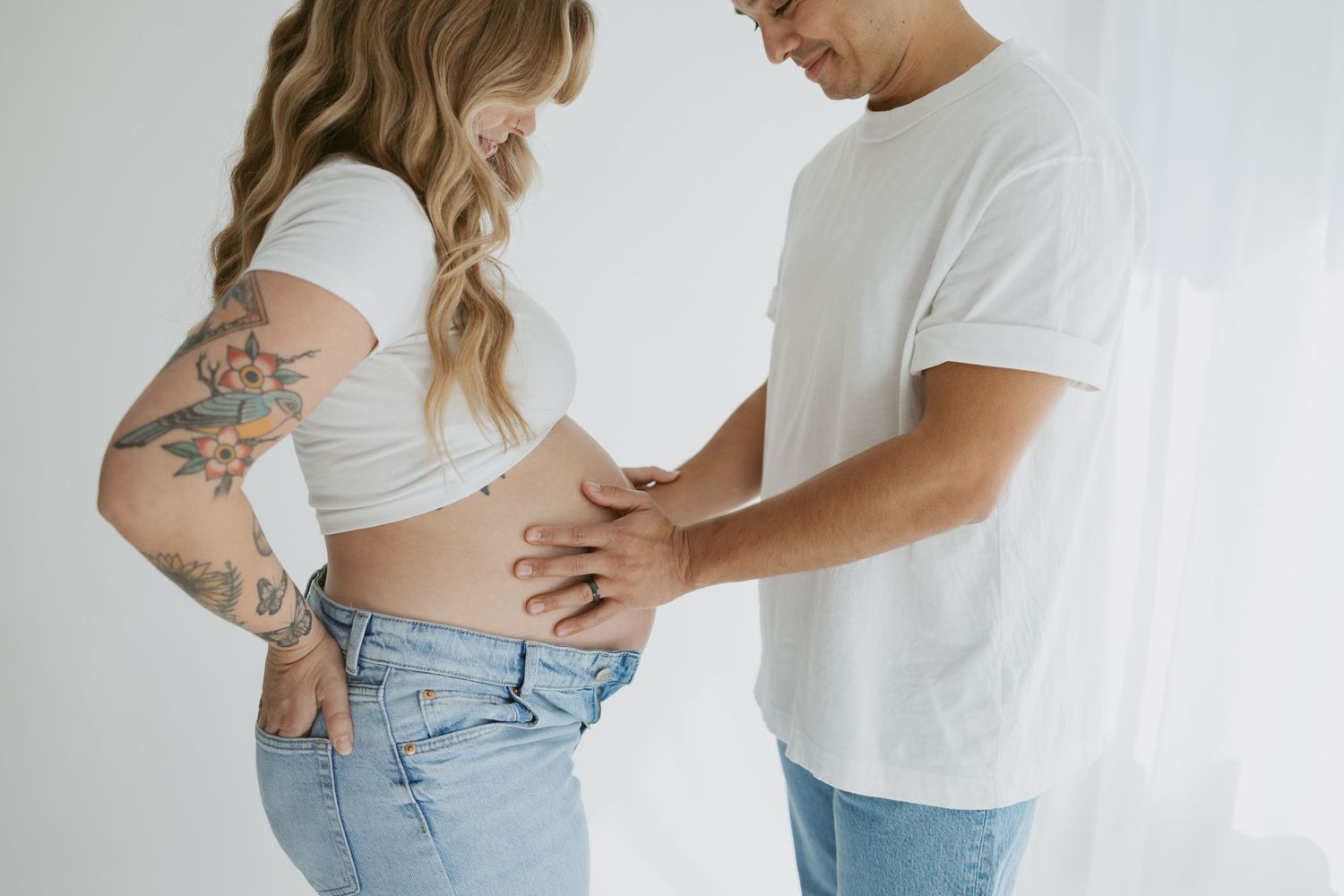 Intimate maternity moment captured as couple in casual wear shows affection.