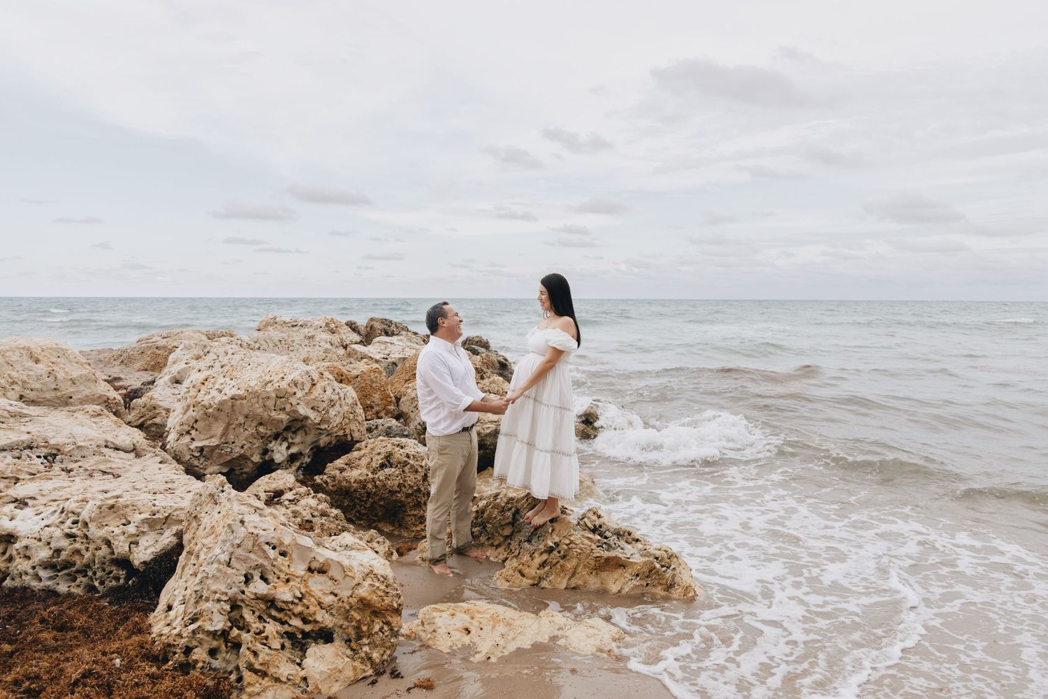 A couple stands on coastal rocks overlooking the ocean waves during an intimate moment.