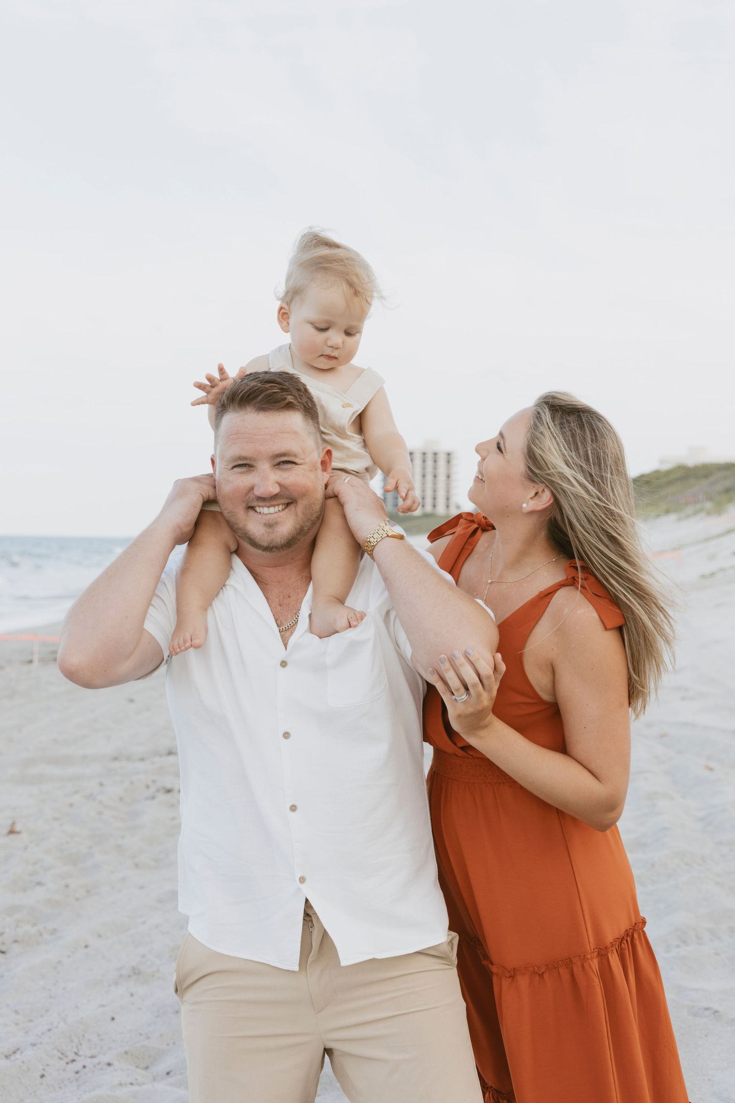 Happy family playing together on sunny beach with child riding on shoulders.