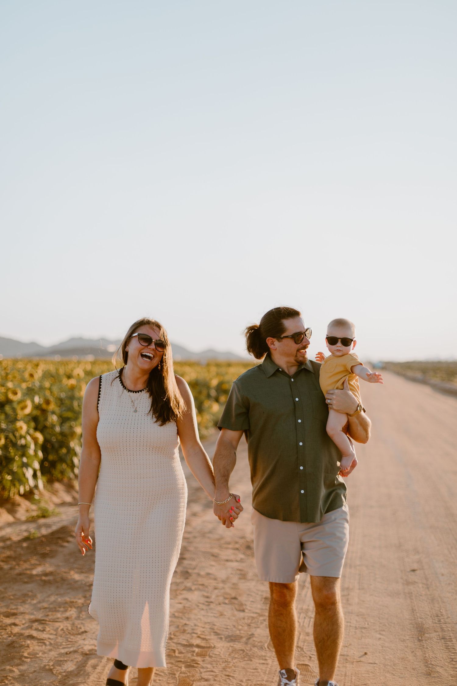 Happy family laughing during sunflower field photo shoot at golden hour