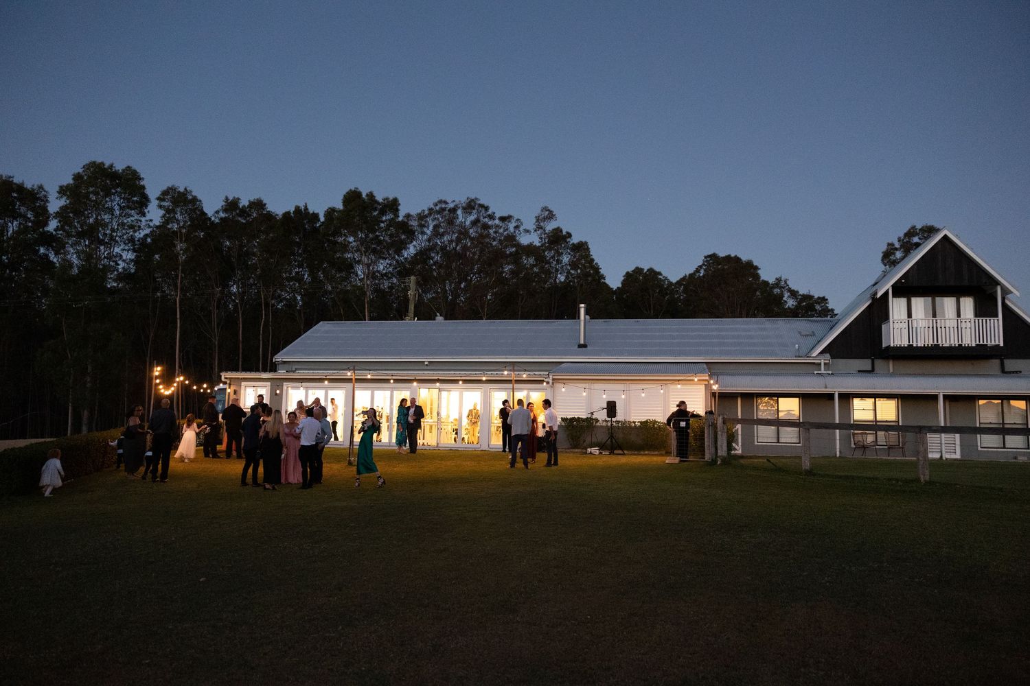 Long white building illuminated at dusk with warm glowing lights and silhouettes visible through windows.