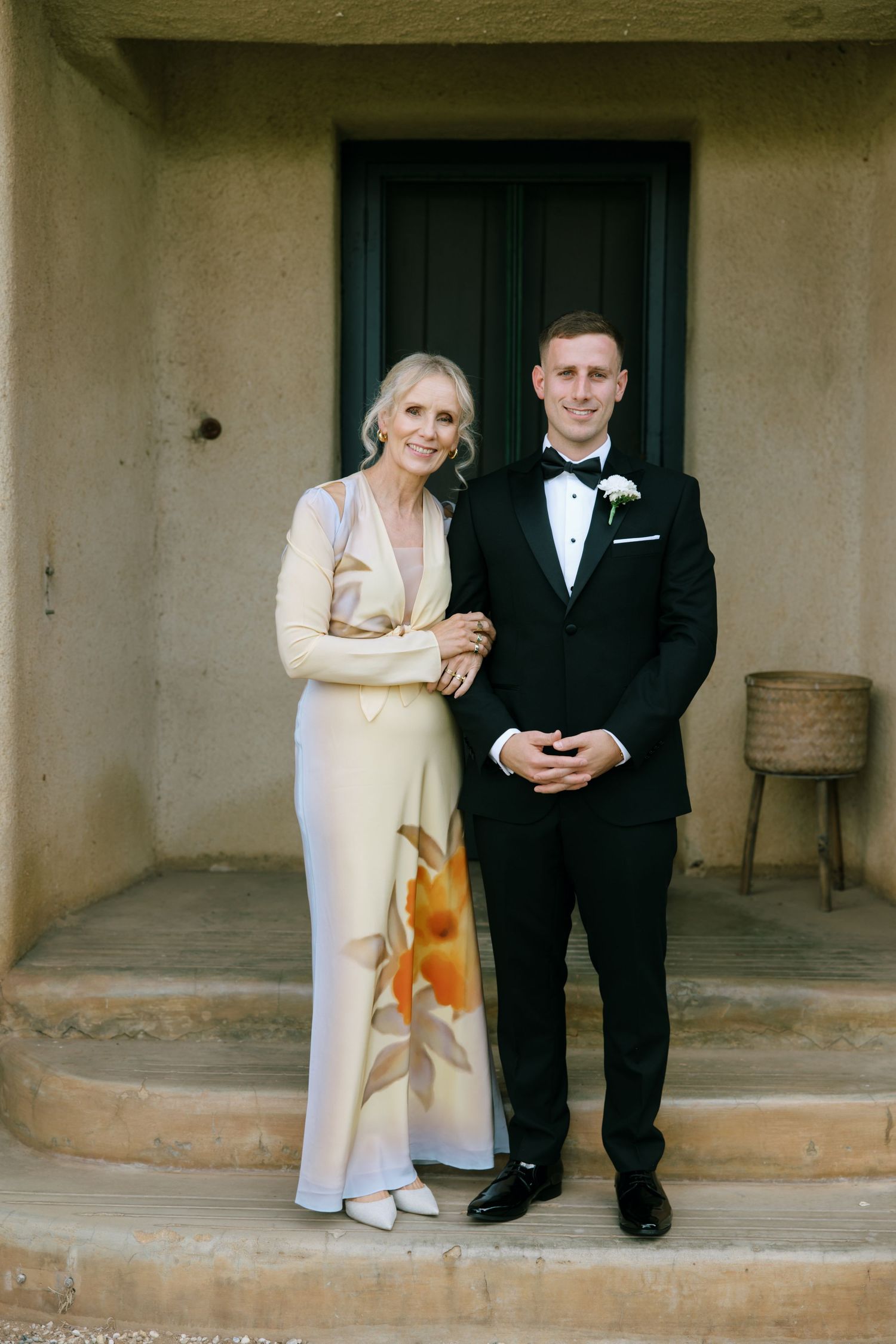 Wedding couple in formal attire sits casually on stone steps with rustic architectural elements.