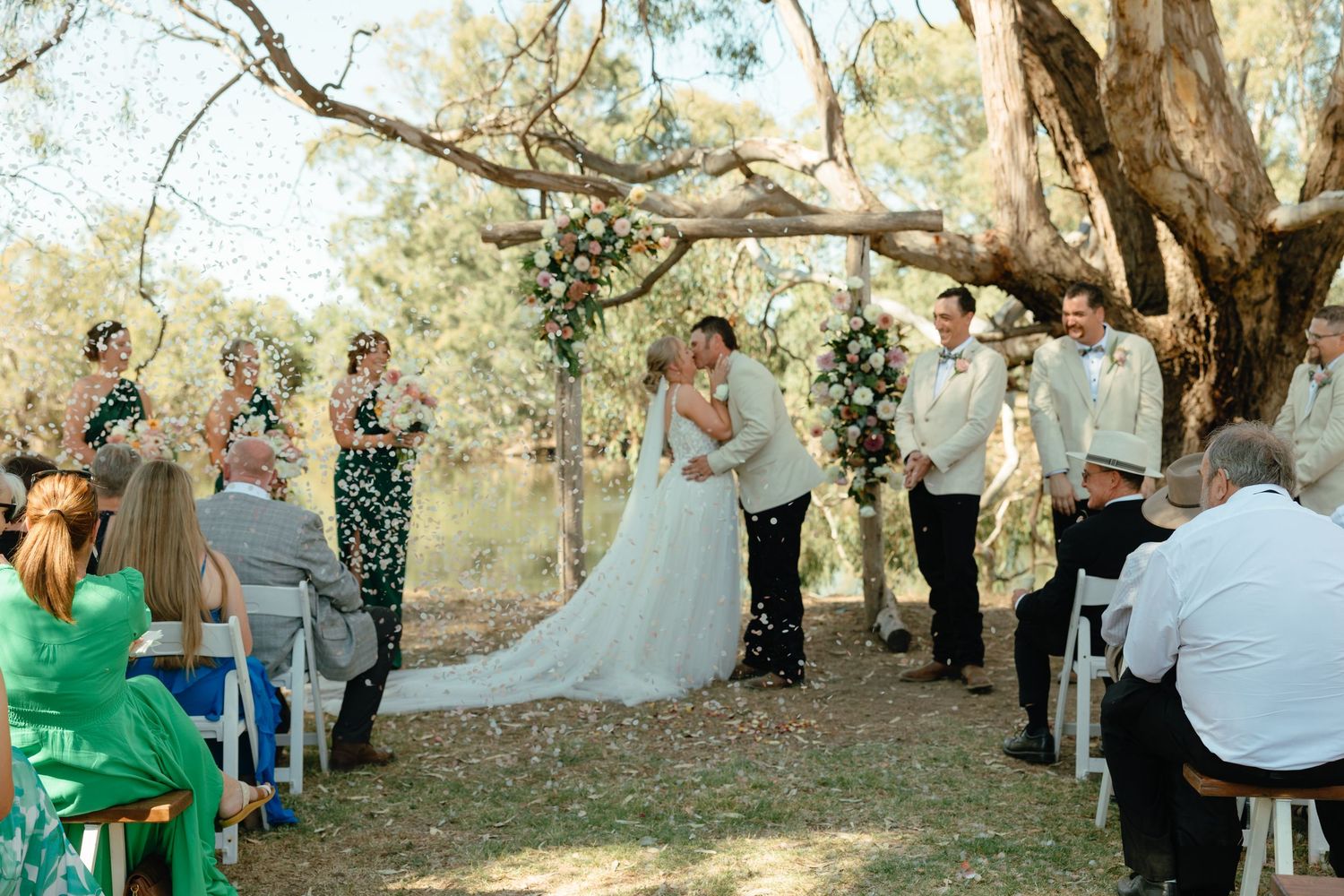 Wedding guests gather beneath towering oak trees draped in Spanish moss during an outdoor ceremony in the woods.