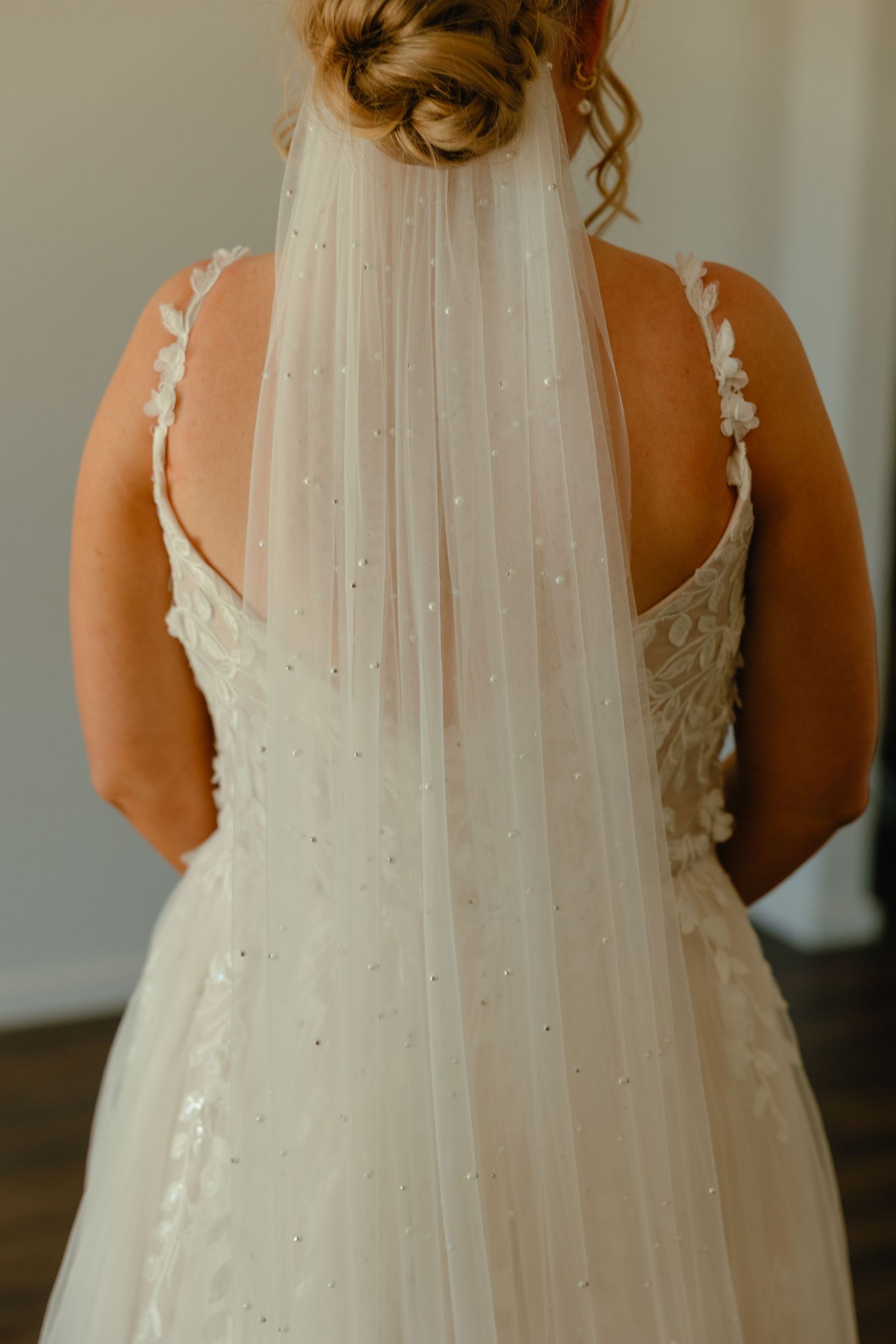 Back view of a bride wearing an elegant white wedding gown with lace straps and sparkly tulle veil.