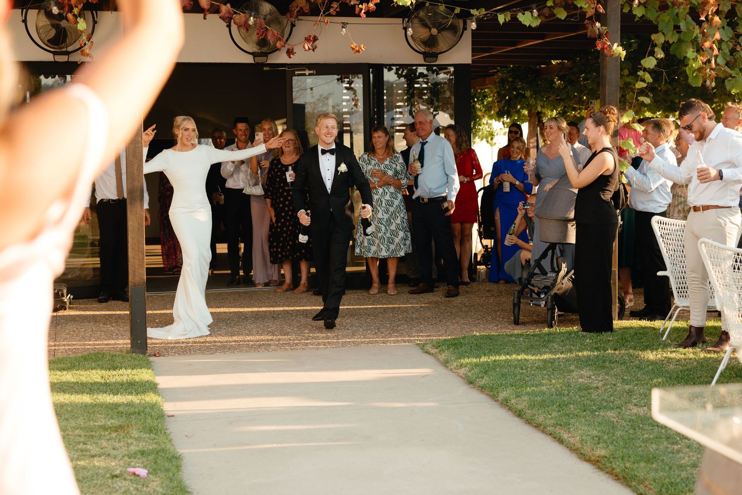 Wedding guests gather outdoors on a walkway at dusk during an evening garden reception celebration.