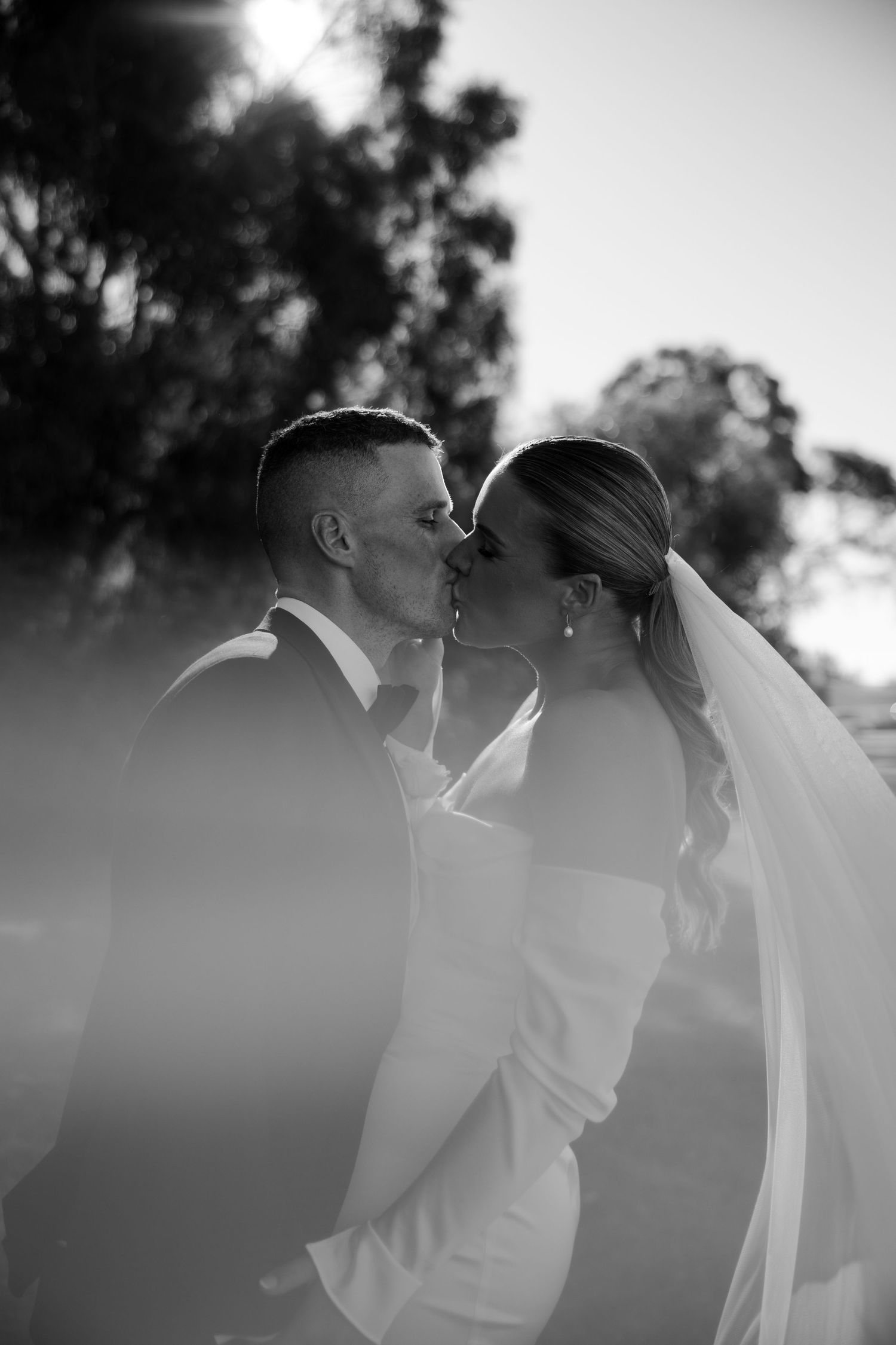 A romantic black and white photo sequence showing a couple sharing intimate kisses at sunset with trees in the background.