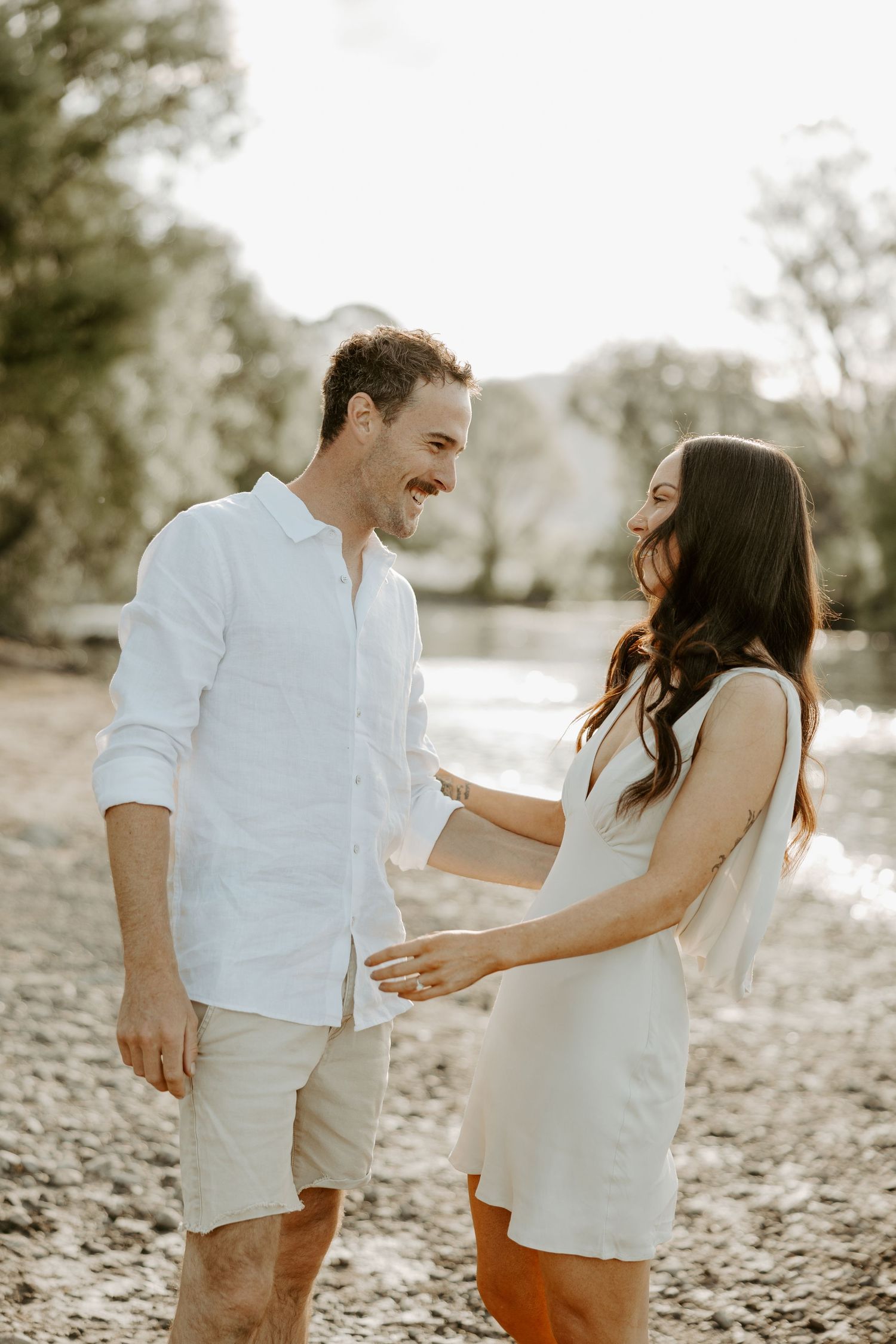 Happy couple laughing together during a sunlit outdoor photoshoot in casual summer attire.