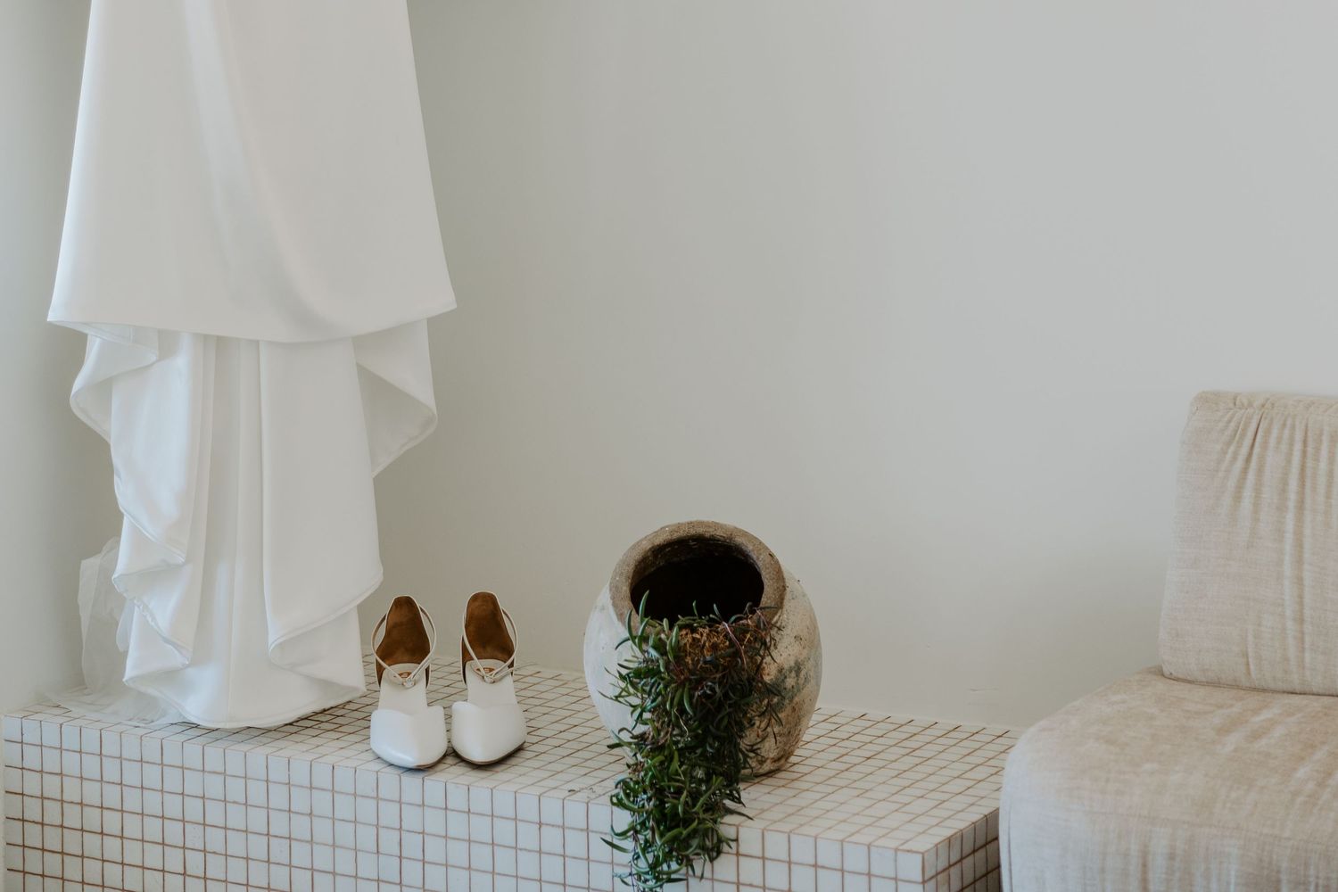 A serene white minimalist bedroom interior with a bed, plants, and natural light streaming through white curtains.