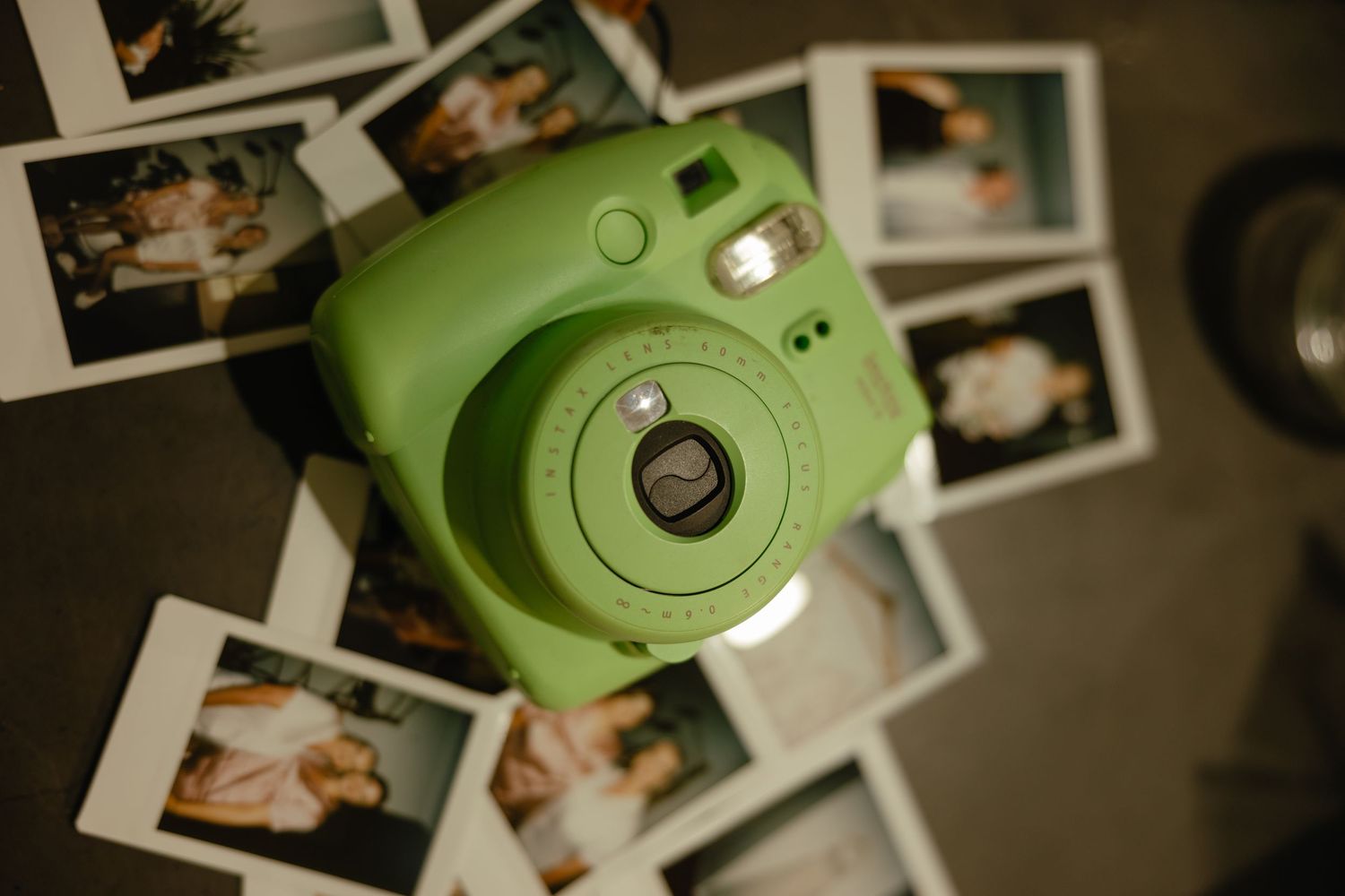 A close-up photo of a green Instax instant camera surrounded by scattered polaroid photographs.