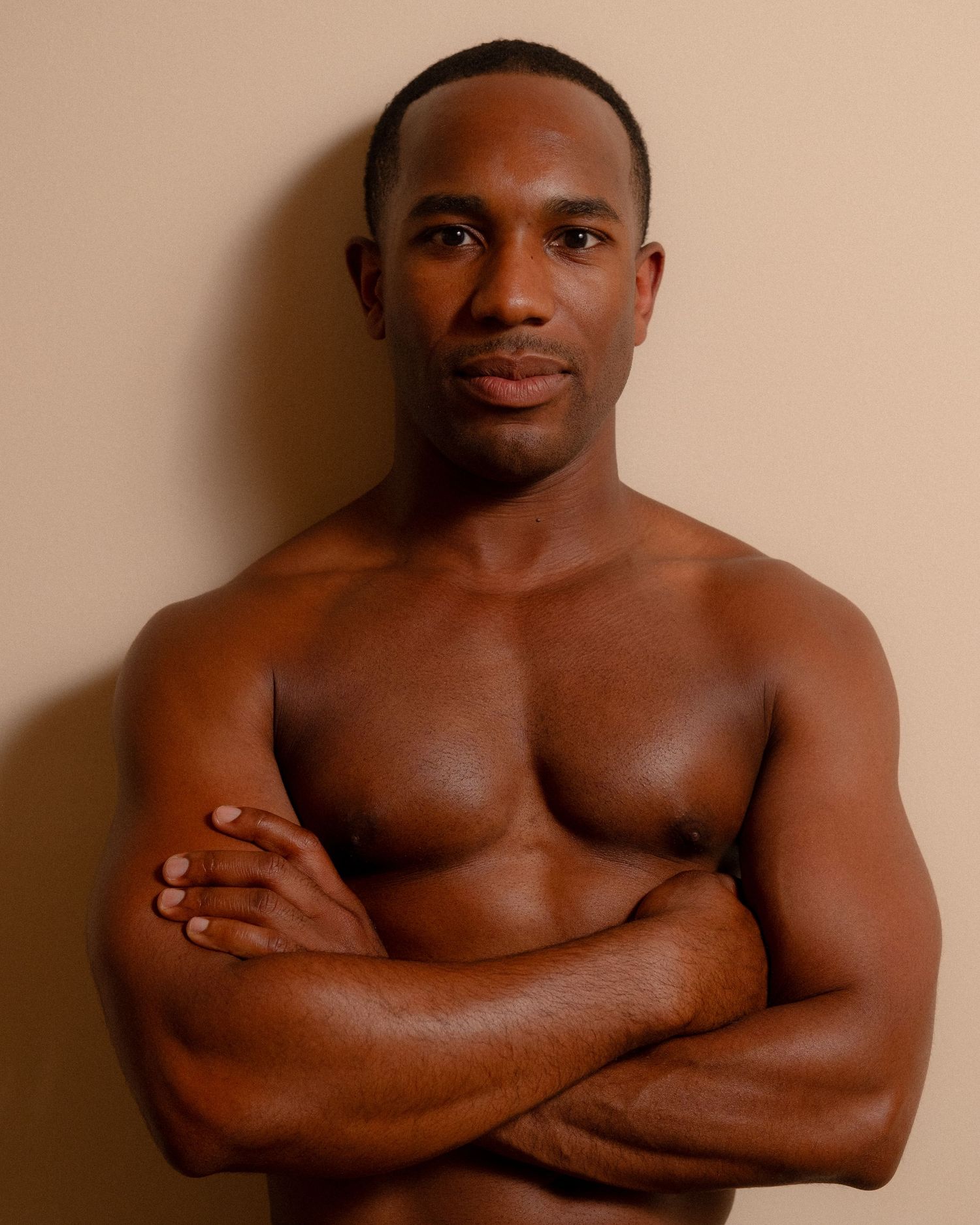 Warm studio portrait of a man with arms crossed.