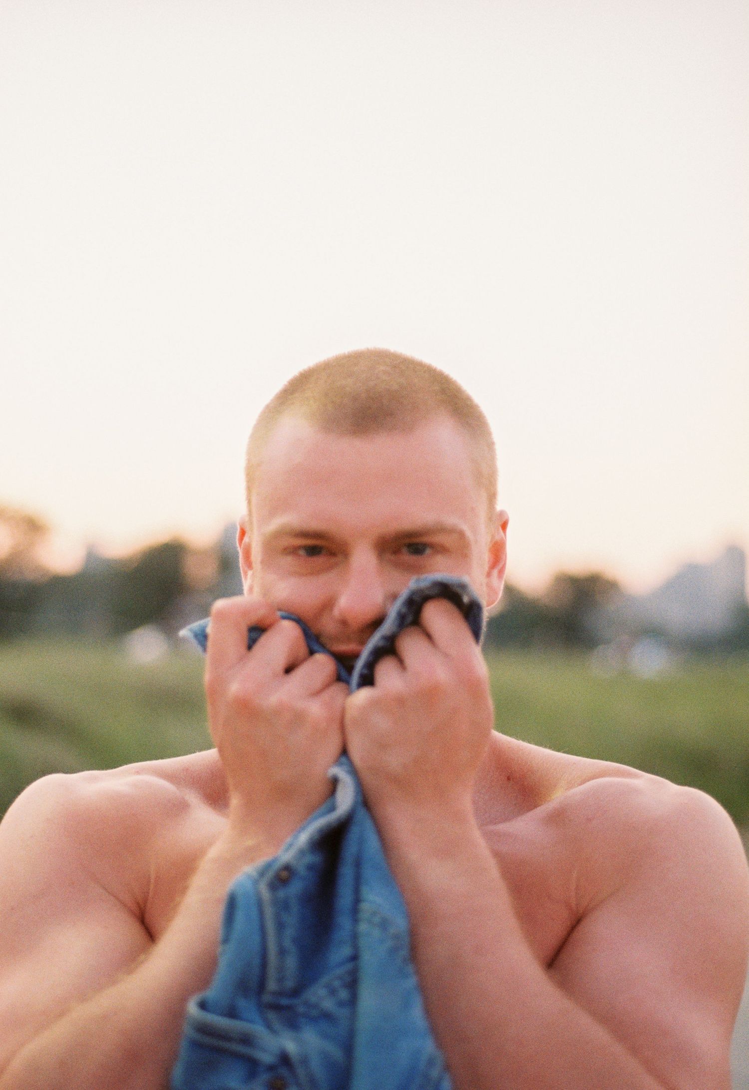 A man standing in front of a sunset with arms too his face looking at the camera on 35mm film.