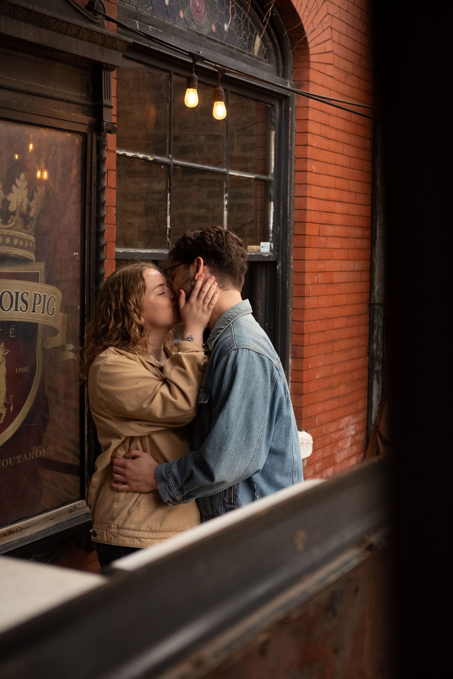 A couple intimately kiss in front of the window of a coffee shop. They are celebrating their engagement.