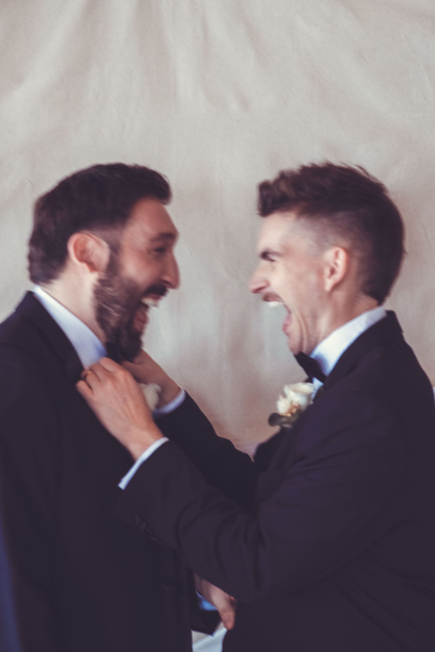 A gay couple laugh as they fix each others ties on 35mm film.