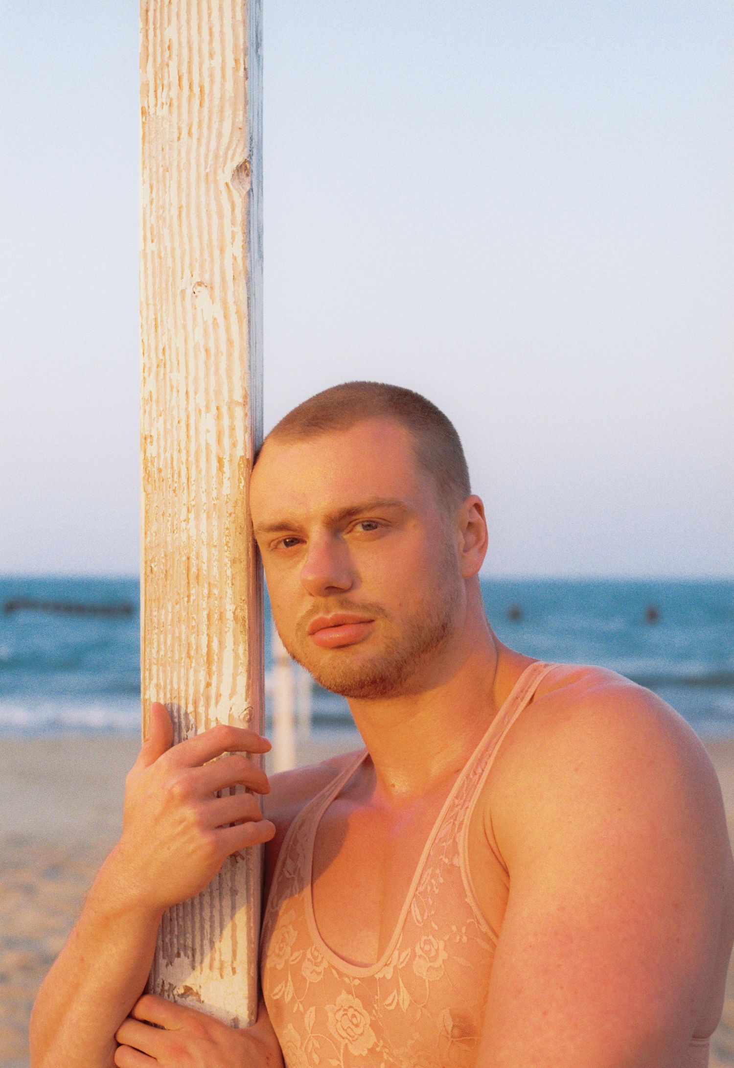 A man in a lace shirt stands against a pole with natural sunlight on 35mm film.