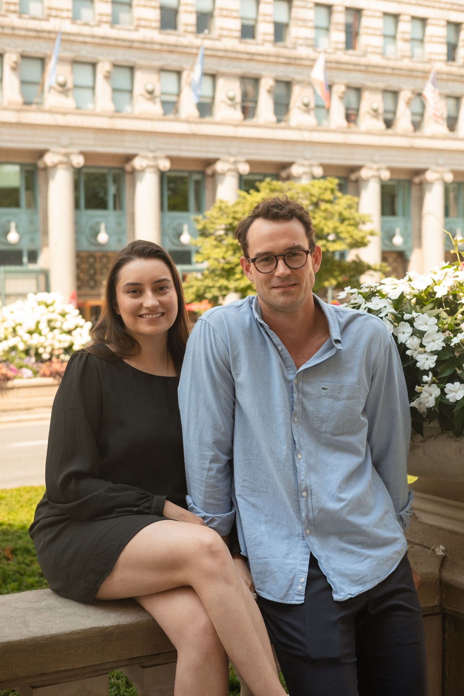 An engaged couple photographed sitting with the building behind them and shot on 35mm film.