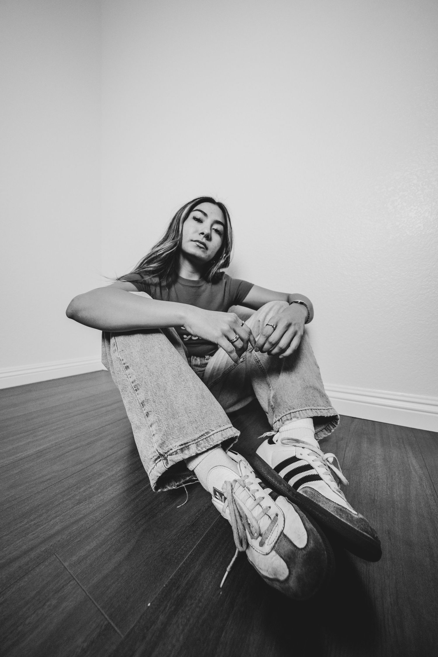 Black and white artistic portrait of someone sitting on wooden floor wearing jeans and sneakers.