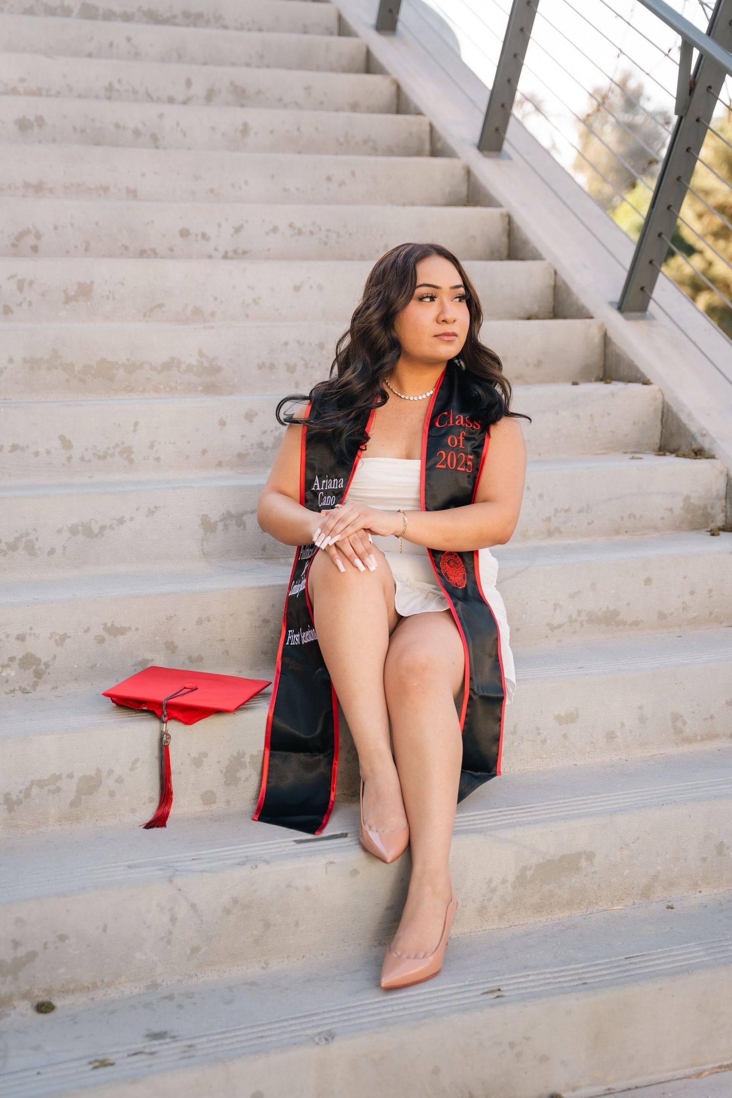 Graduate poses on concrete stairs wearing a black and red graduation stole.