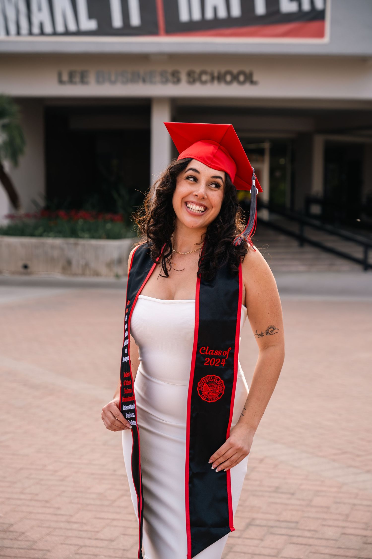 Graduate in red cap poses cheerfully outside Lee Business School building.