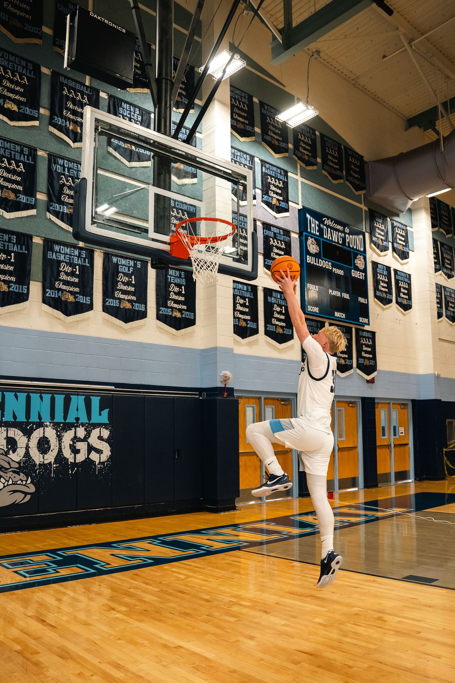 Player in white uniform jumping for layup beneath basketball hoop.
