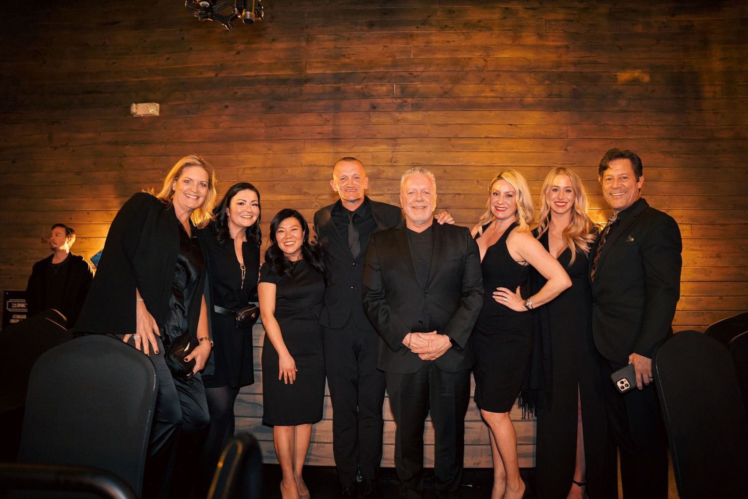 Group photo of event participants posing against rustic wooden wall backdrop.