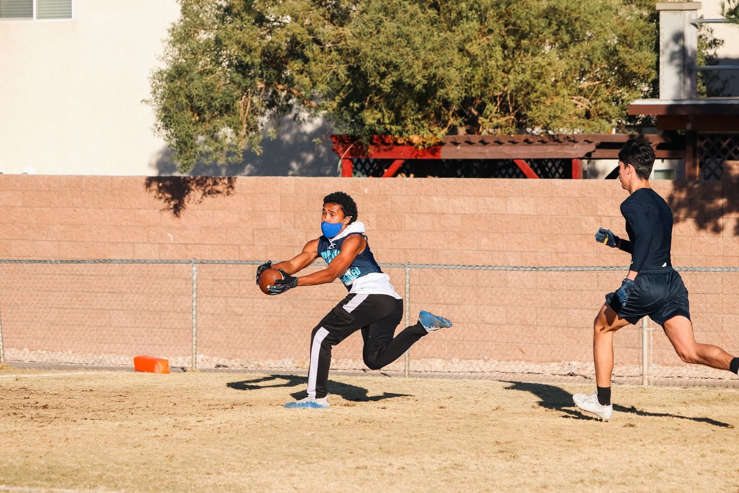 Player running with a football during practice drill on a dirt field.