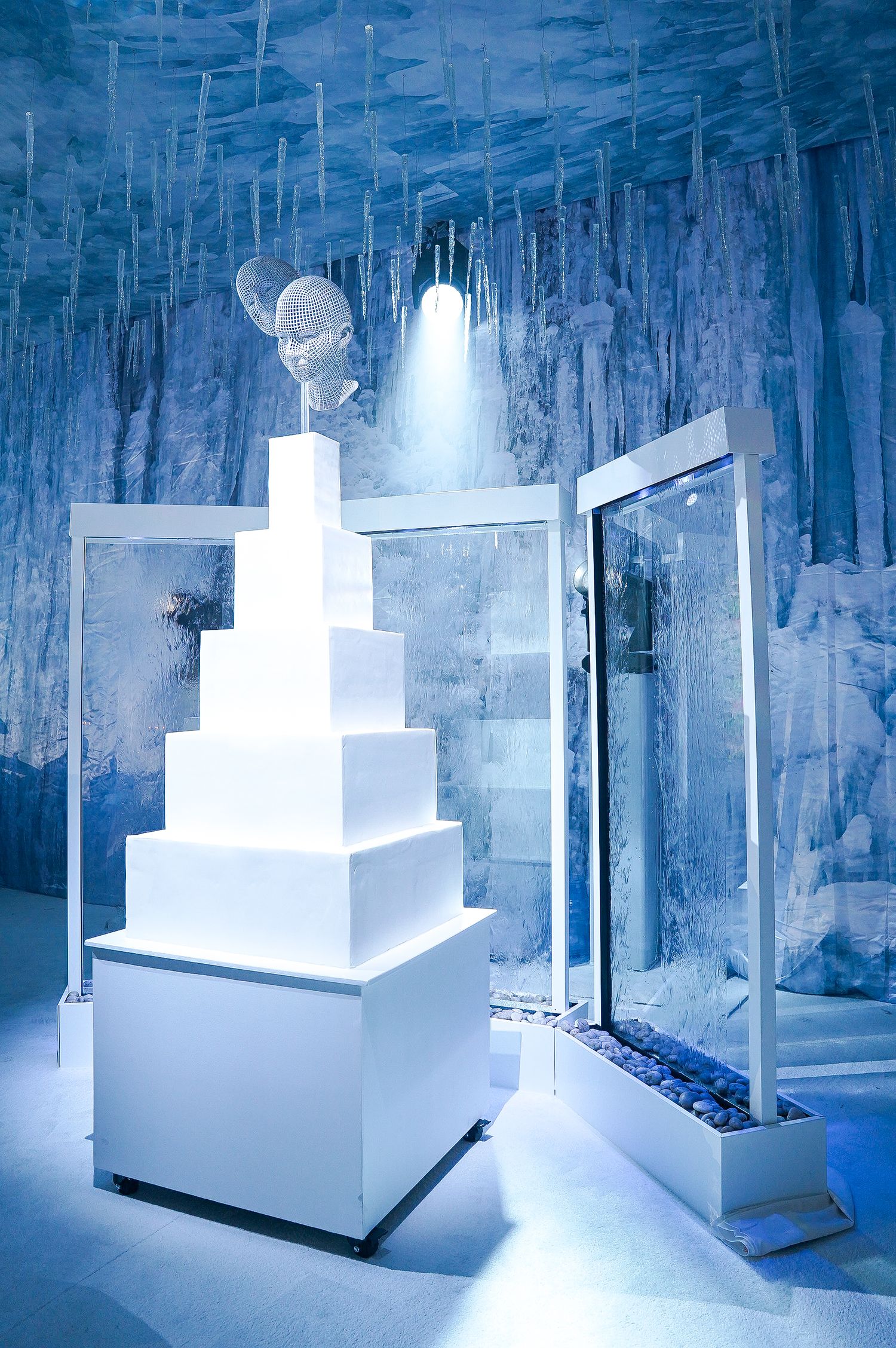 Modern white tiered display stand in ice-themed room with dramatic lighting.