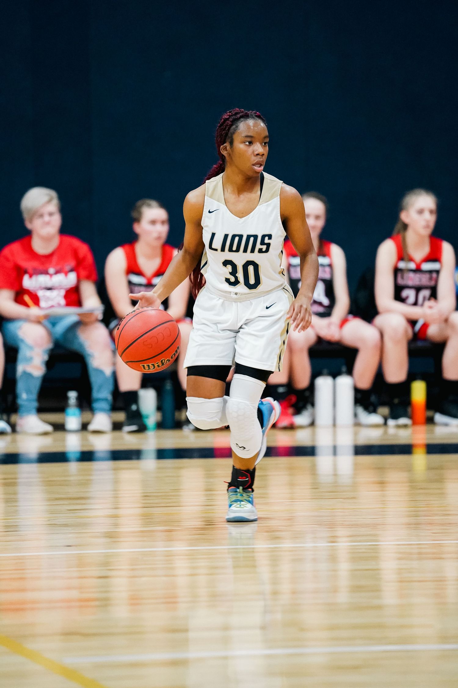 Basketball player dribbles down court in Lions white uniform during competitive game.