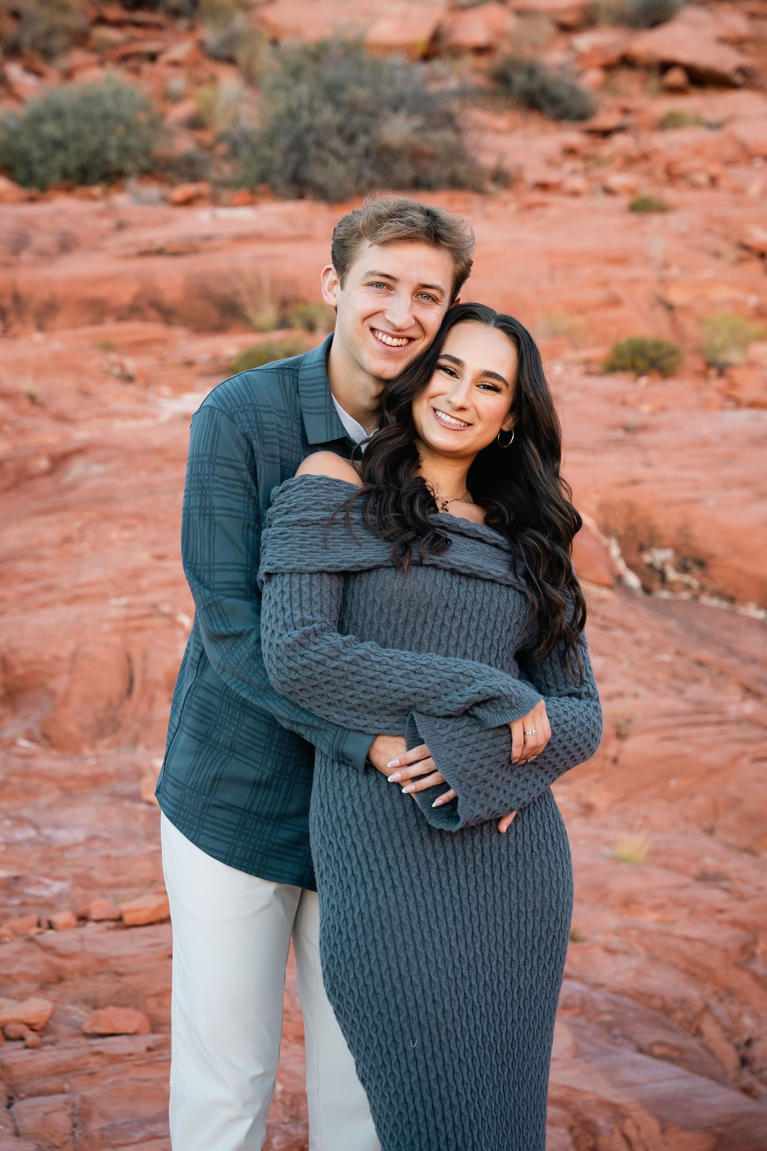 A happy couple sharing an affectionate moment against vibrant red rock formations.
