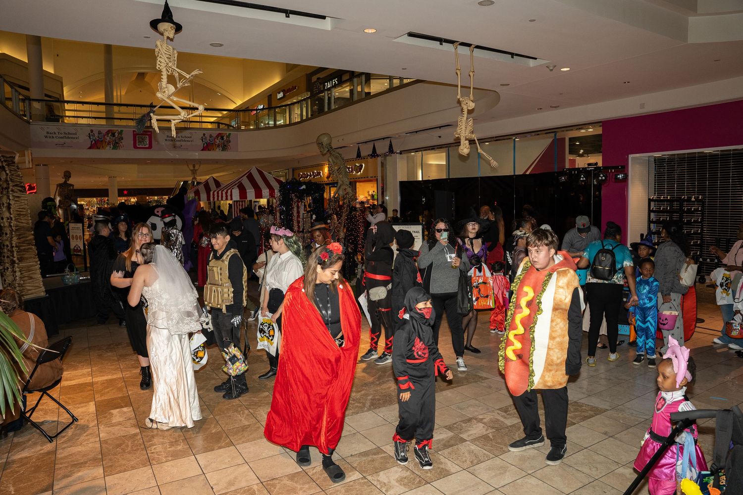 A crowded indoor Halloween event showing people in various costumes gathering in a mall space.