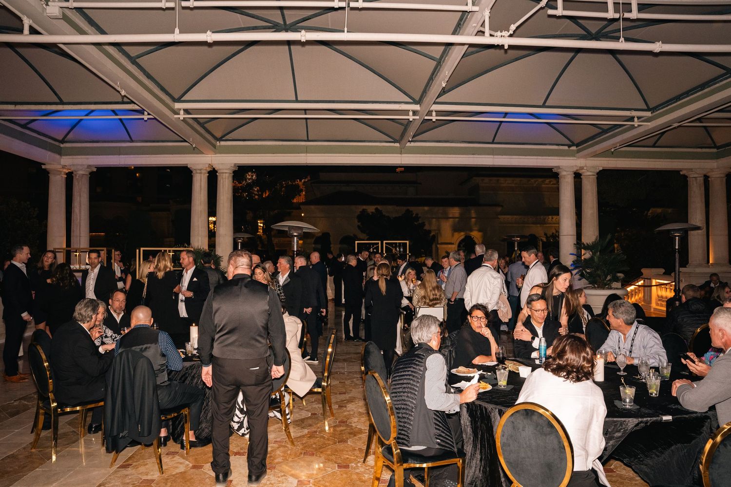 Guests mingle and socialize at an elegant evening event in a covered outdoor venue.