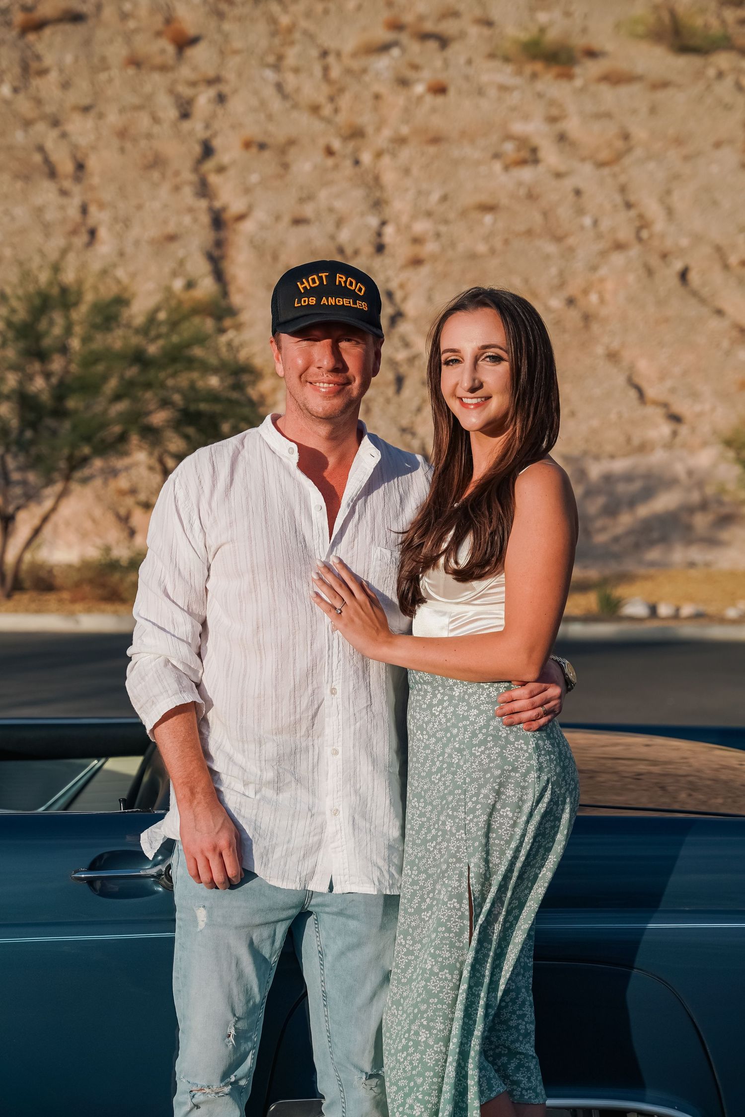 Happy couple sharing tender moments beside their classic blue car in the desert.