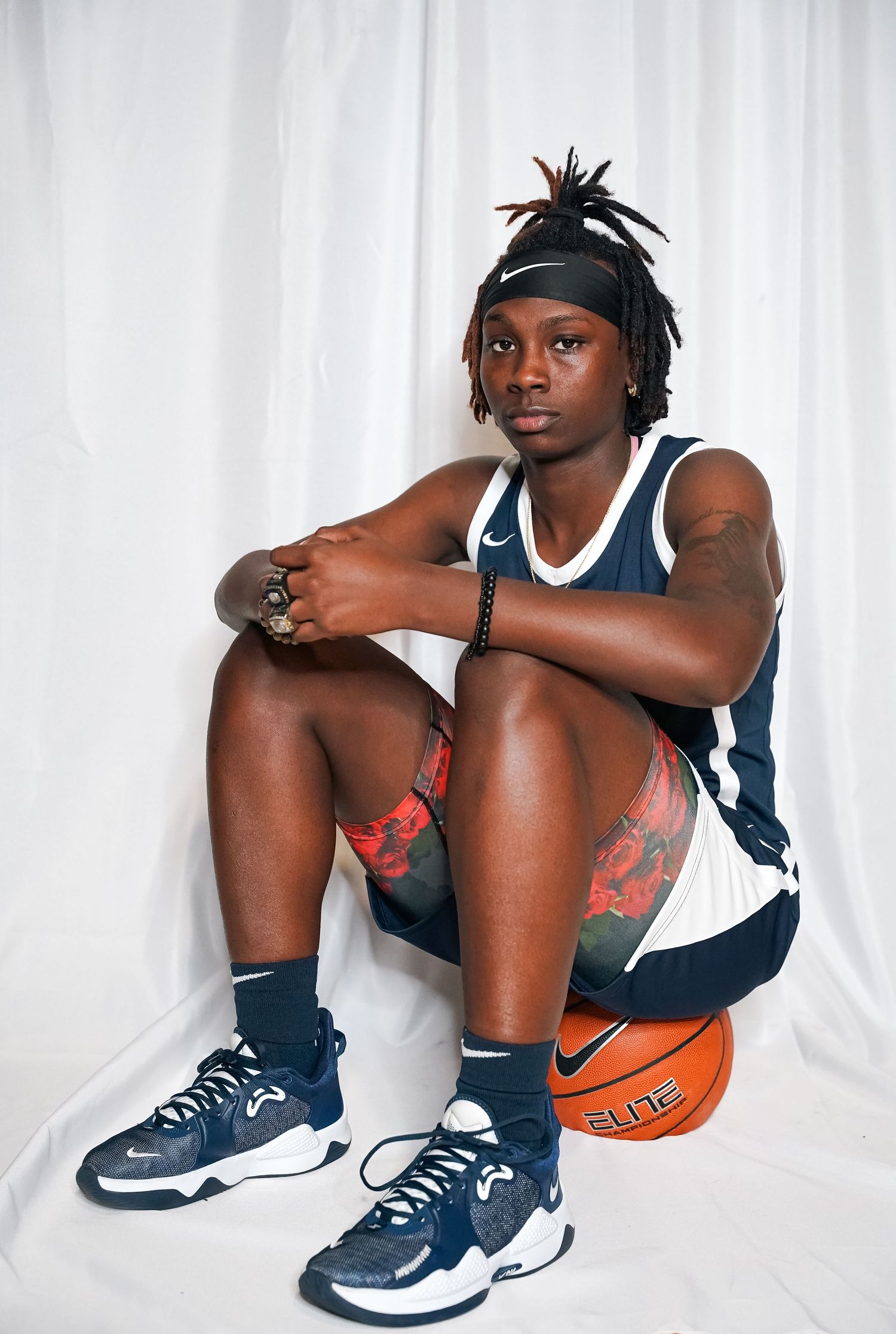 Basketball player in navy uniform sits with Nike ball wearing headband.