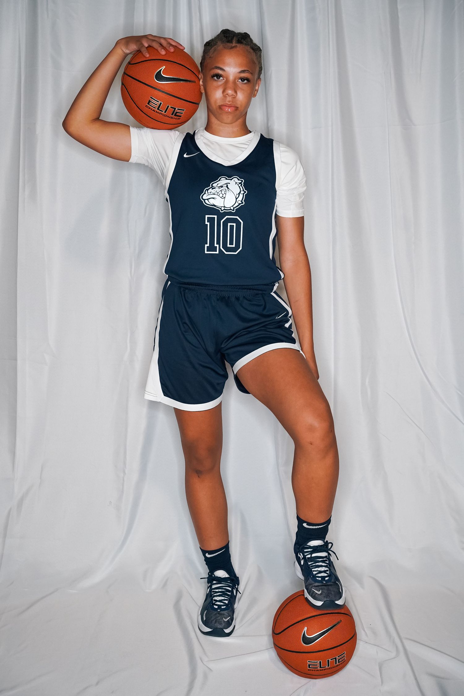Basketball player in navy and white uniform number 10 poses with ball during photo shoot.