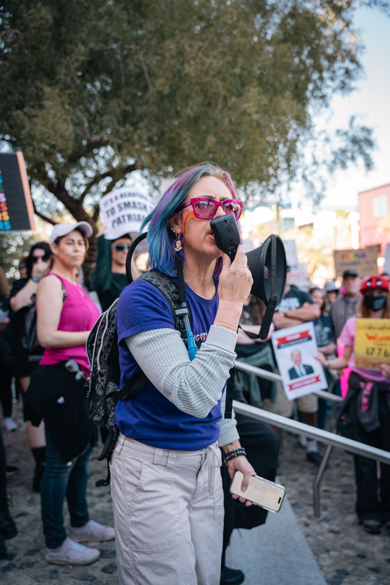 Protesters gather at a rally with signs and megaphones during a daytime demonstration.