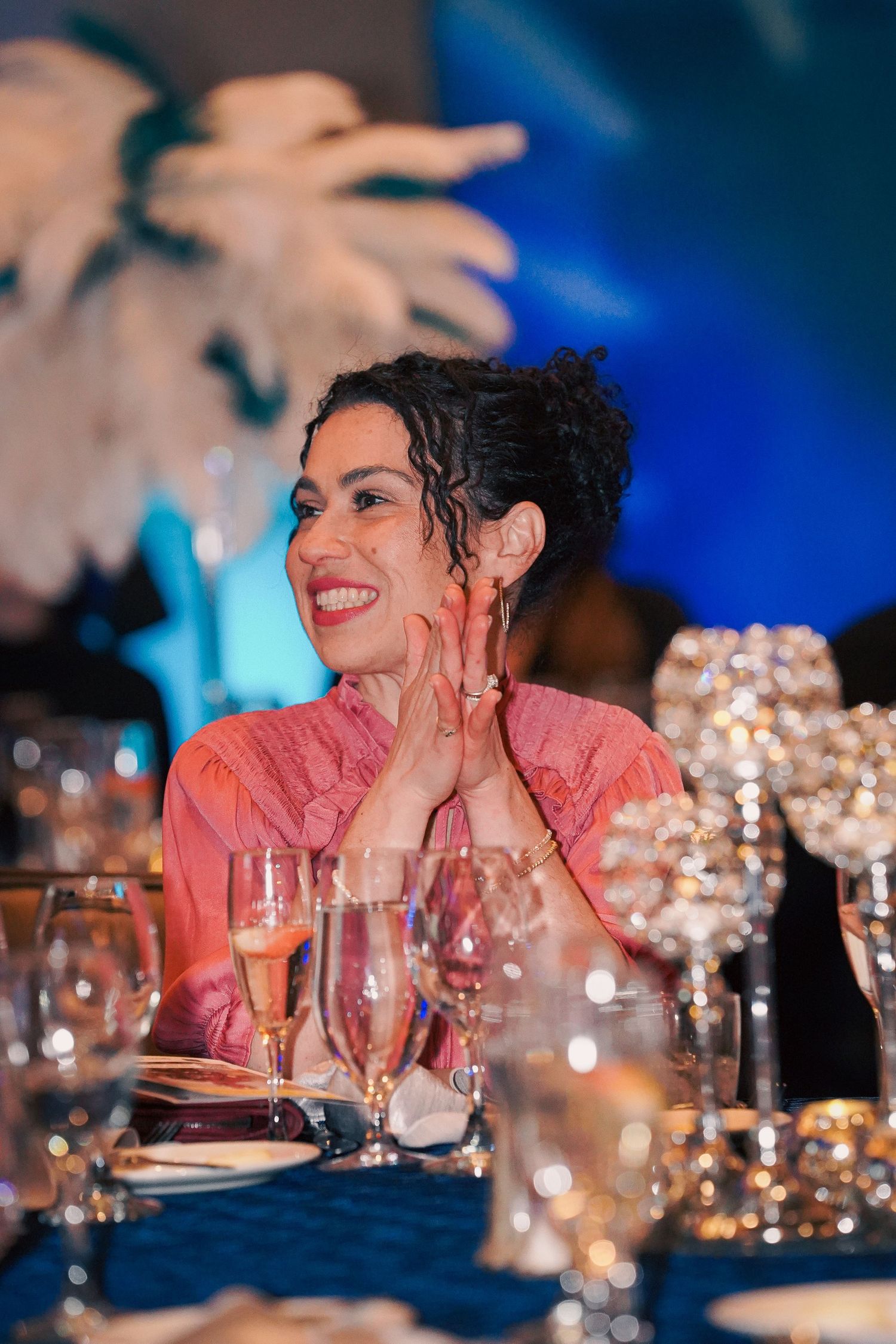 Guest in coral dress enjoys formal dinner event with elegant table settings.