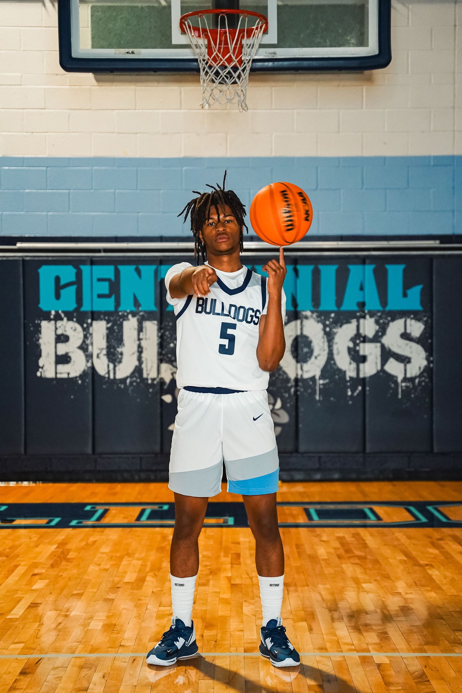 Basketball player holds ball while standing on wooden court with school branding visible.