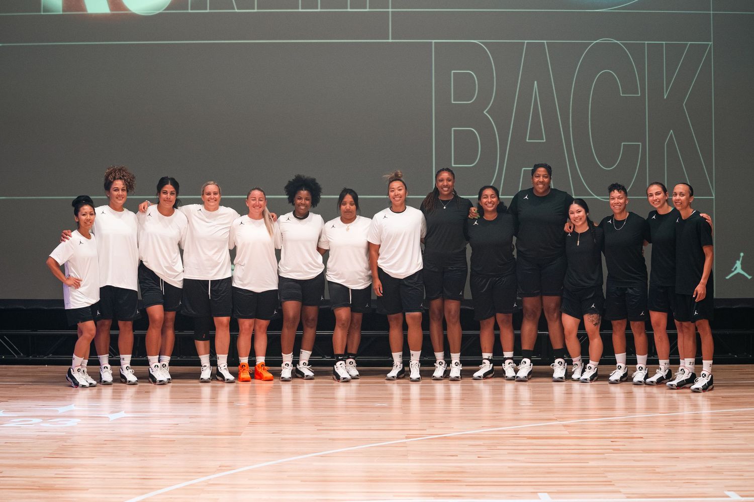 Team photo of basketball players lined up in white and black uniforms on wooden court.