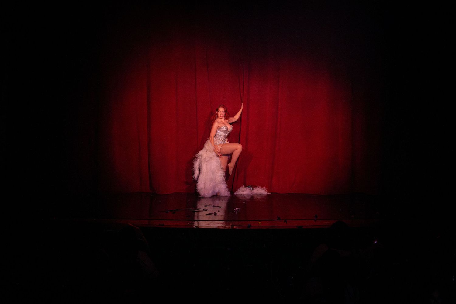 A performer in a pink costume dances under dramatic spotlighting against a red curtain backdrop.